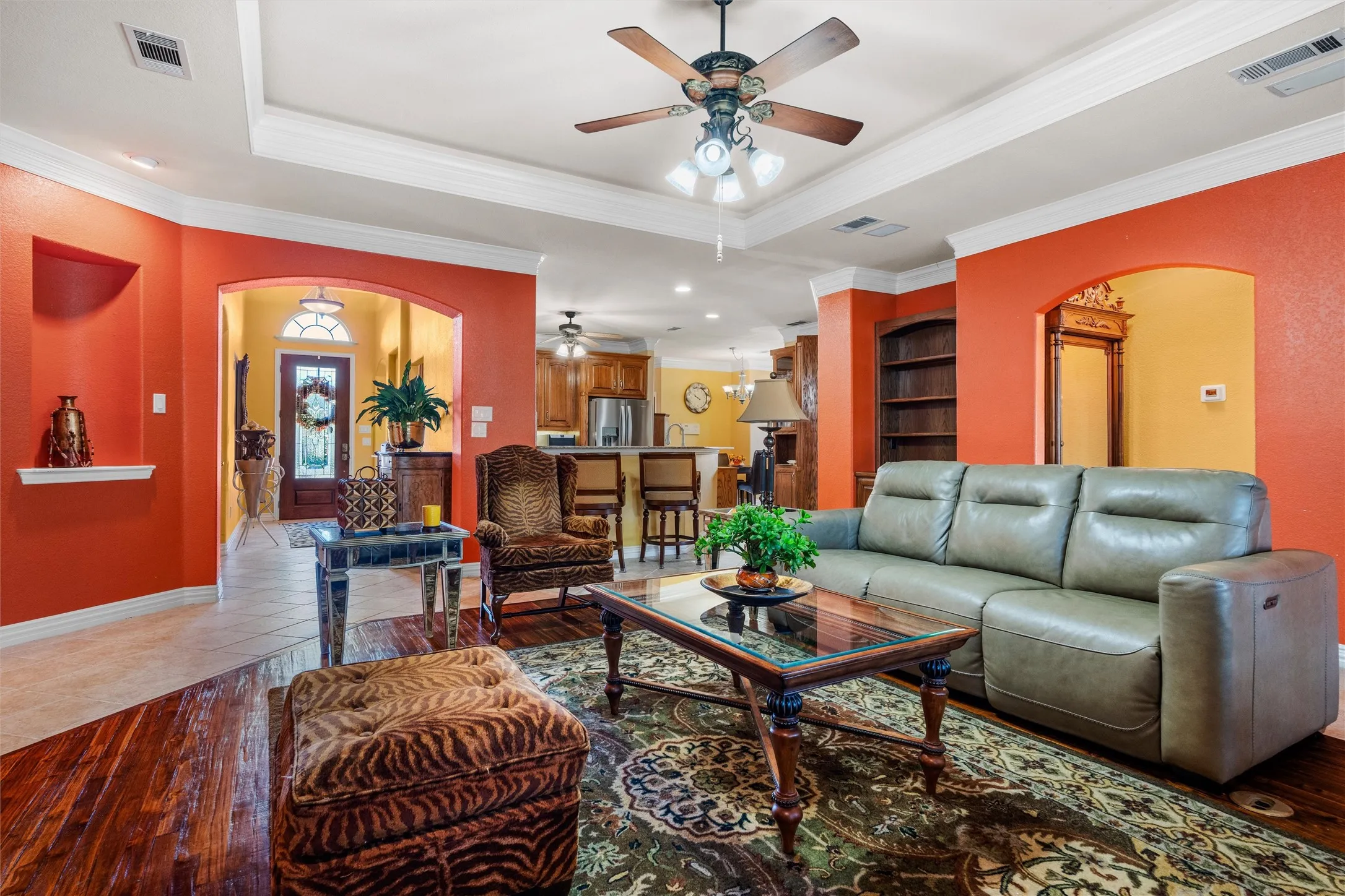 Teak wood flooring, recessed ceiling with crown molding, built-in shelving, arched doorways, and a ceiling fan with light fixture