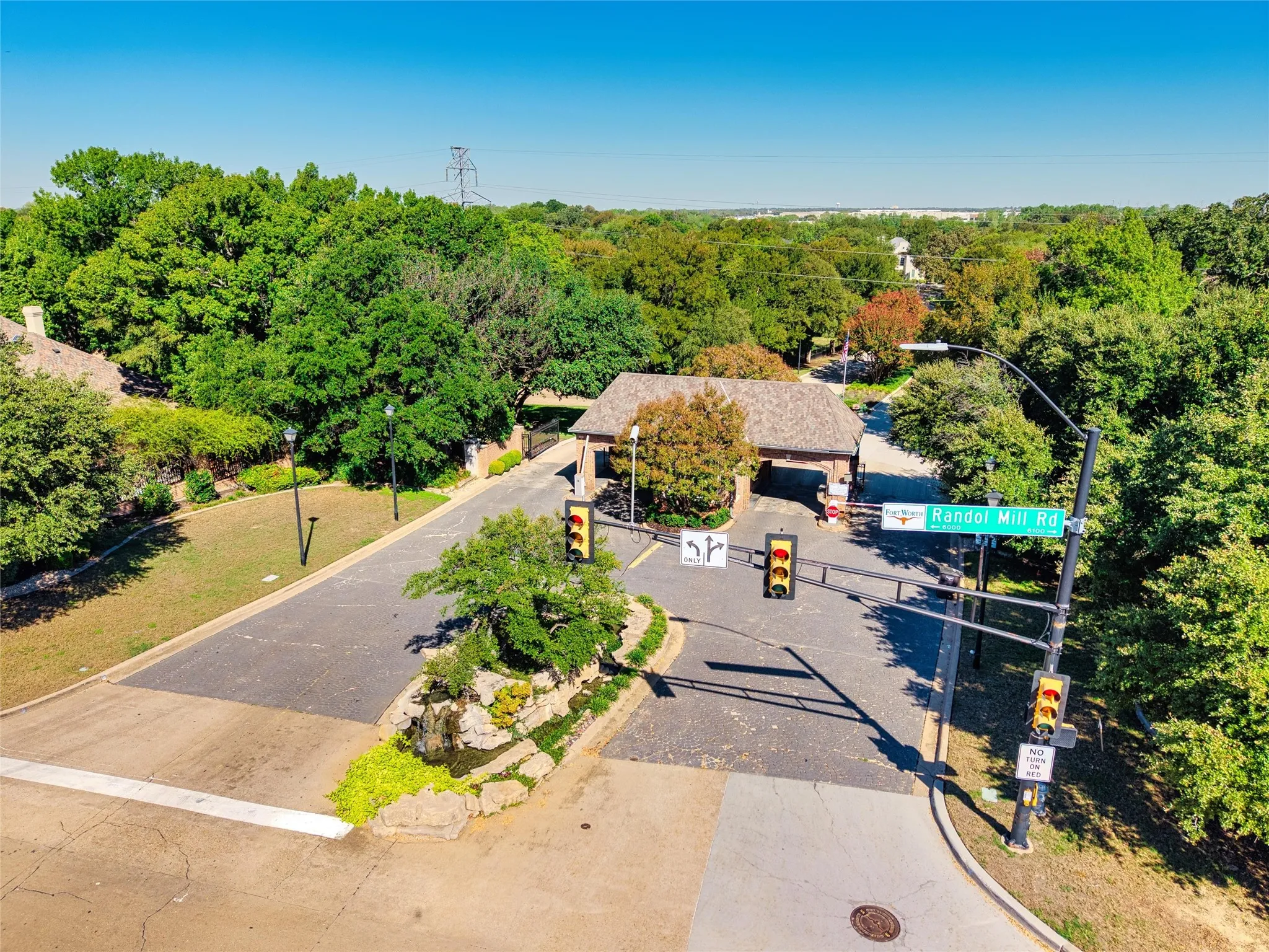 24 Hr Security gated community entrance with a stone-clad guardhouse, mature trees, and a landscaped rock feature