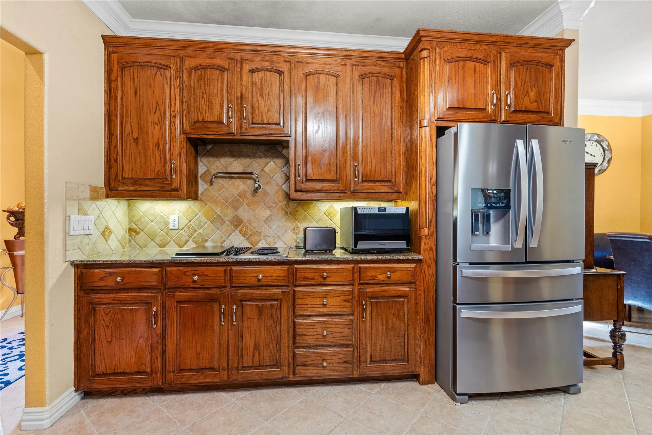 Wood-finish cabinetry with crown molding, tiled backsplash, built-in electic cooktop