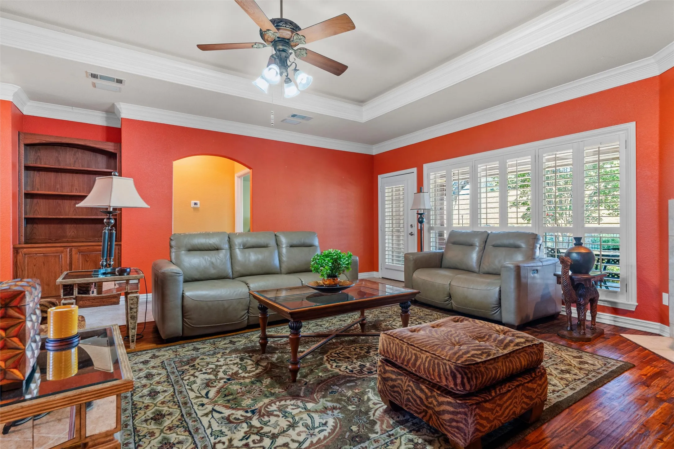 Tray ceiling with crown molding, built in wooden shelving, and a ceiling fan with integrated lighting
