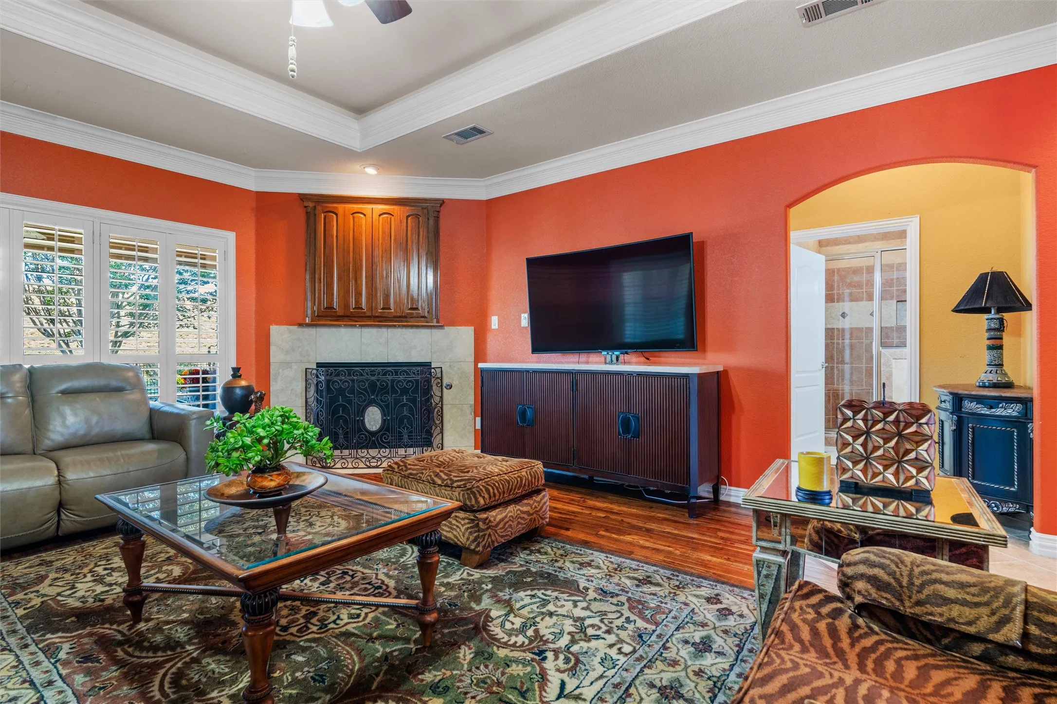 Tray ceiling, Teak wood flooring, built-in fireplace with stone, wood cabinetry, and interior archway