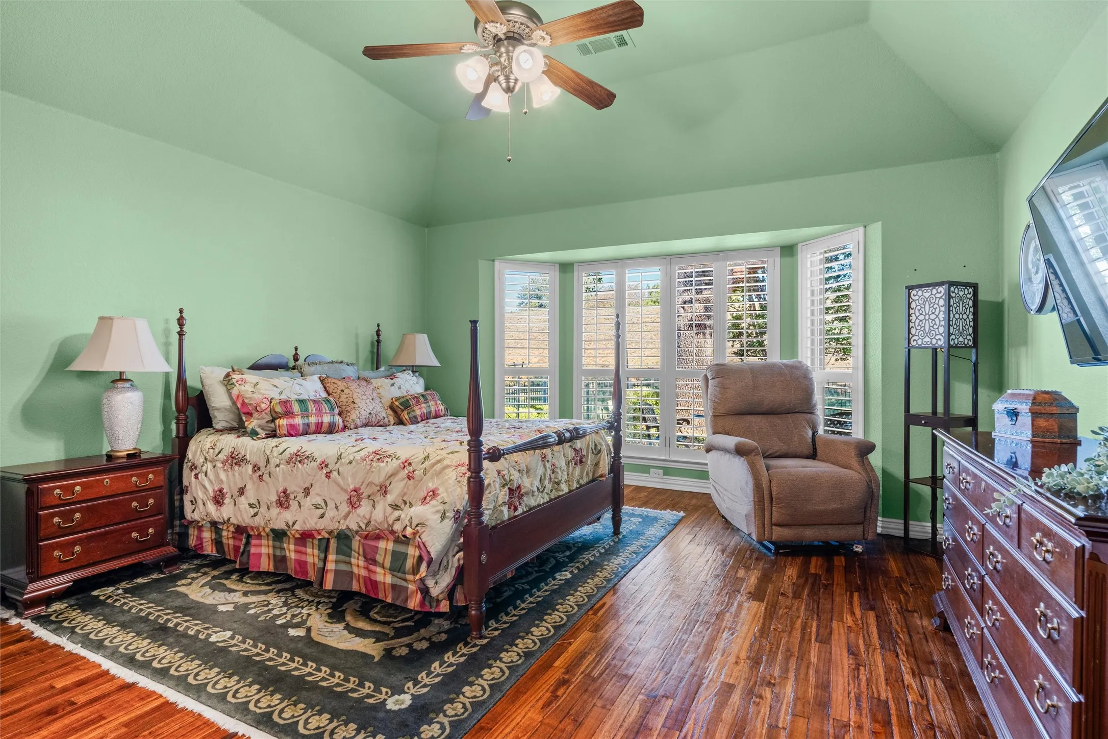Primary Bedroom with vaulted ceiling a ceiling fan, bay window with plantation shutters, and Teak wood flooring