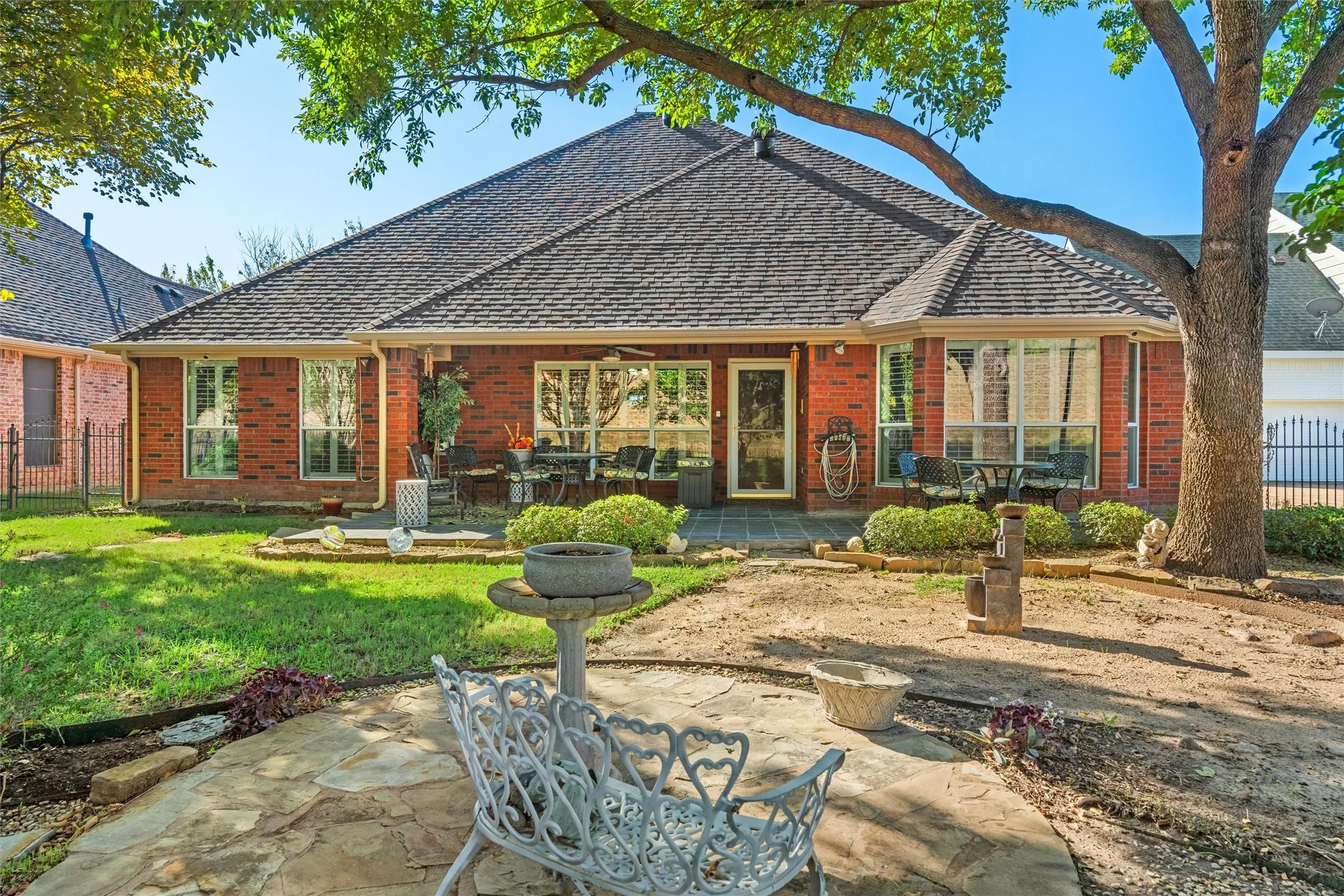 Red brick exterior with a shingle roof, featuring multiple windows, a stone patio, and a grass lawn