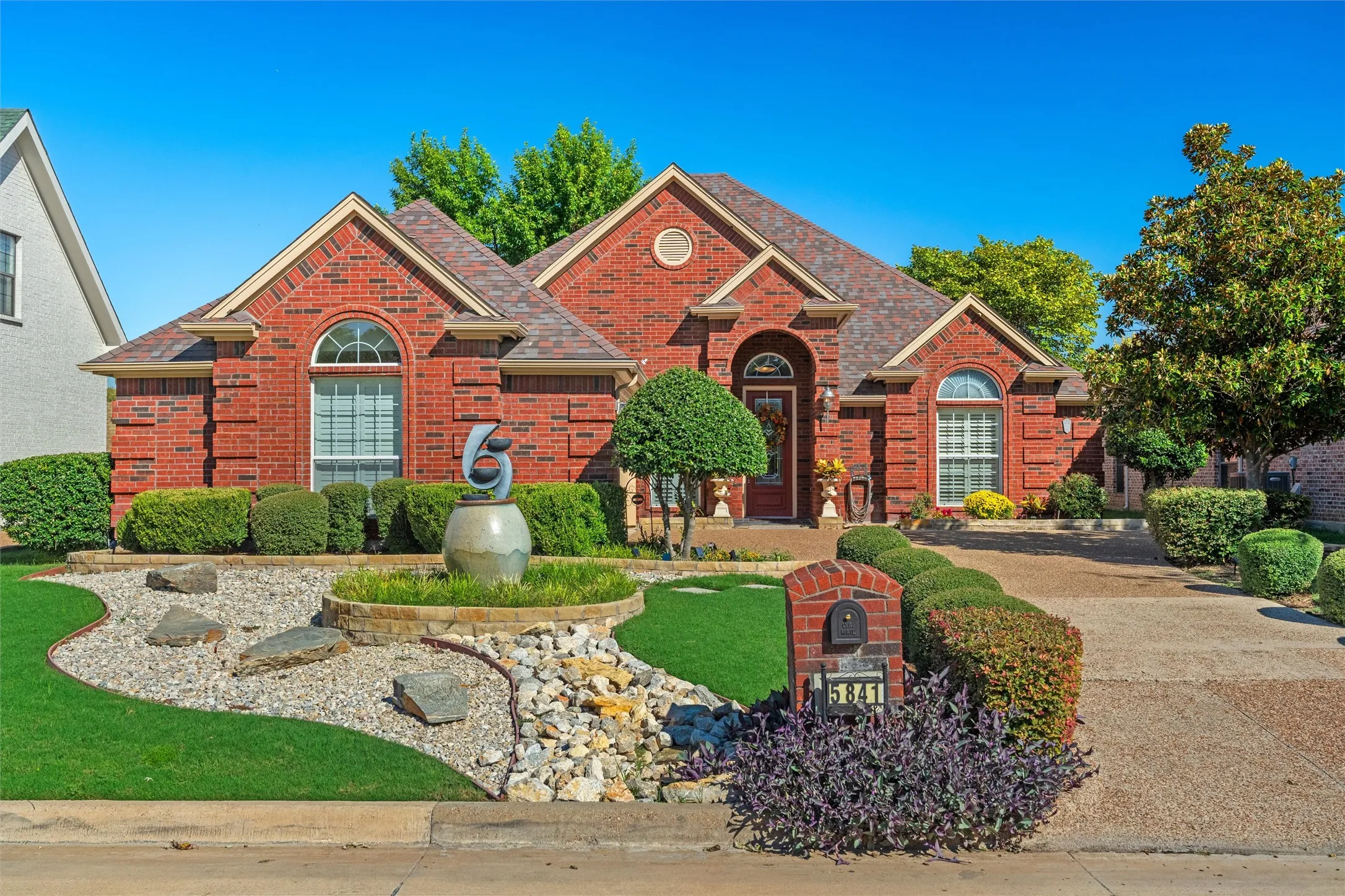 Red brick exterior with arched windows, a multi-level roofline, and established landscaping featuring a decorative fountain