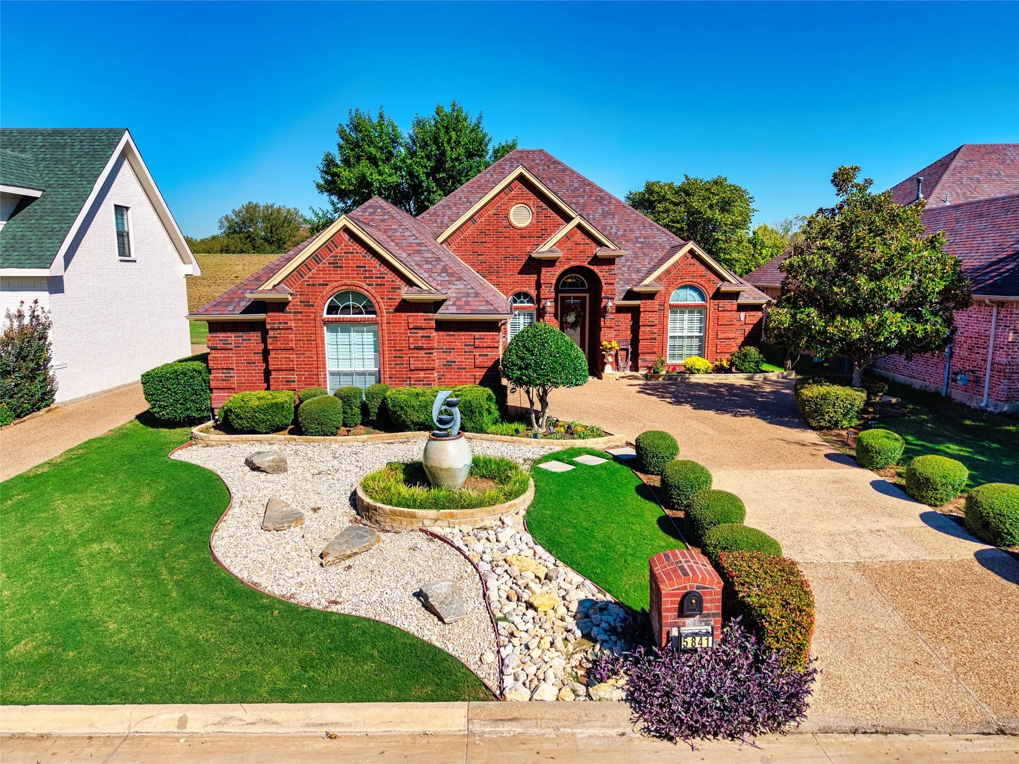 Brick exterior with arched window, landscaped front yard, swing driveway, and mature shrubbery