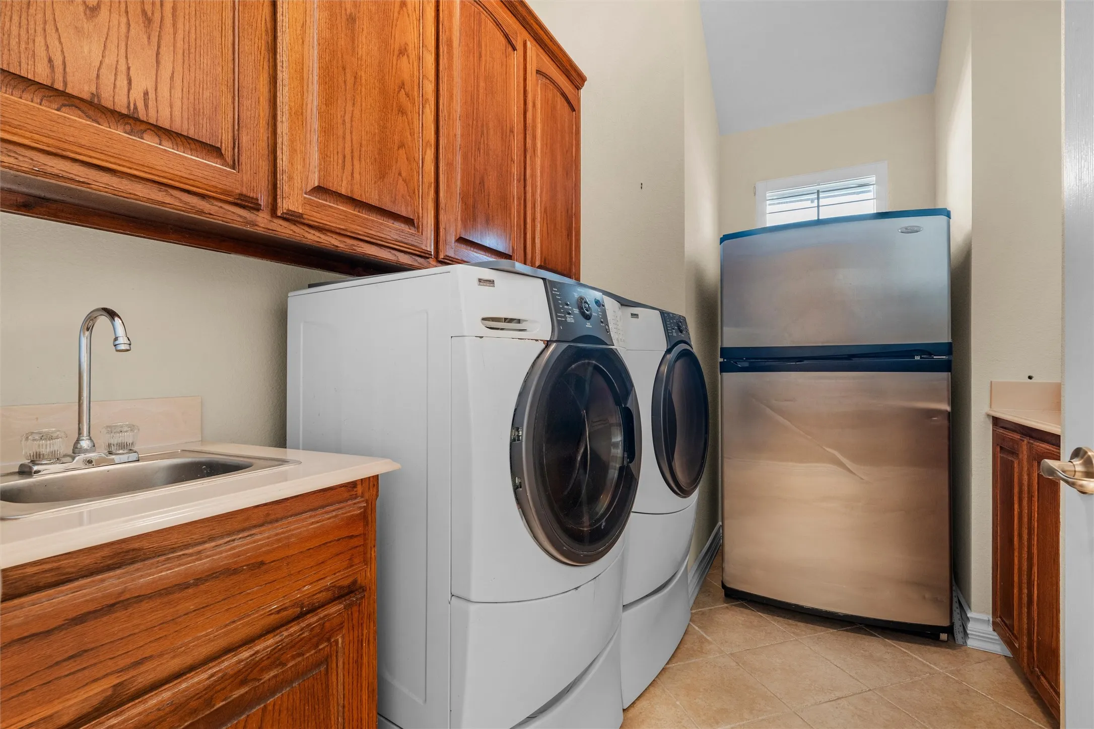 Laundry area with wood cabinetry, tiled flooring, and a utility sink