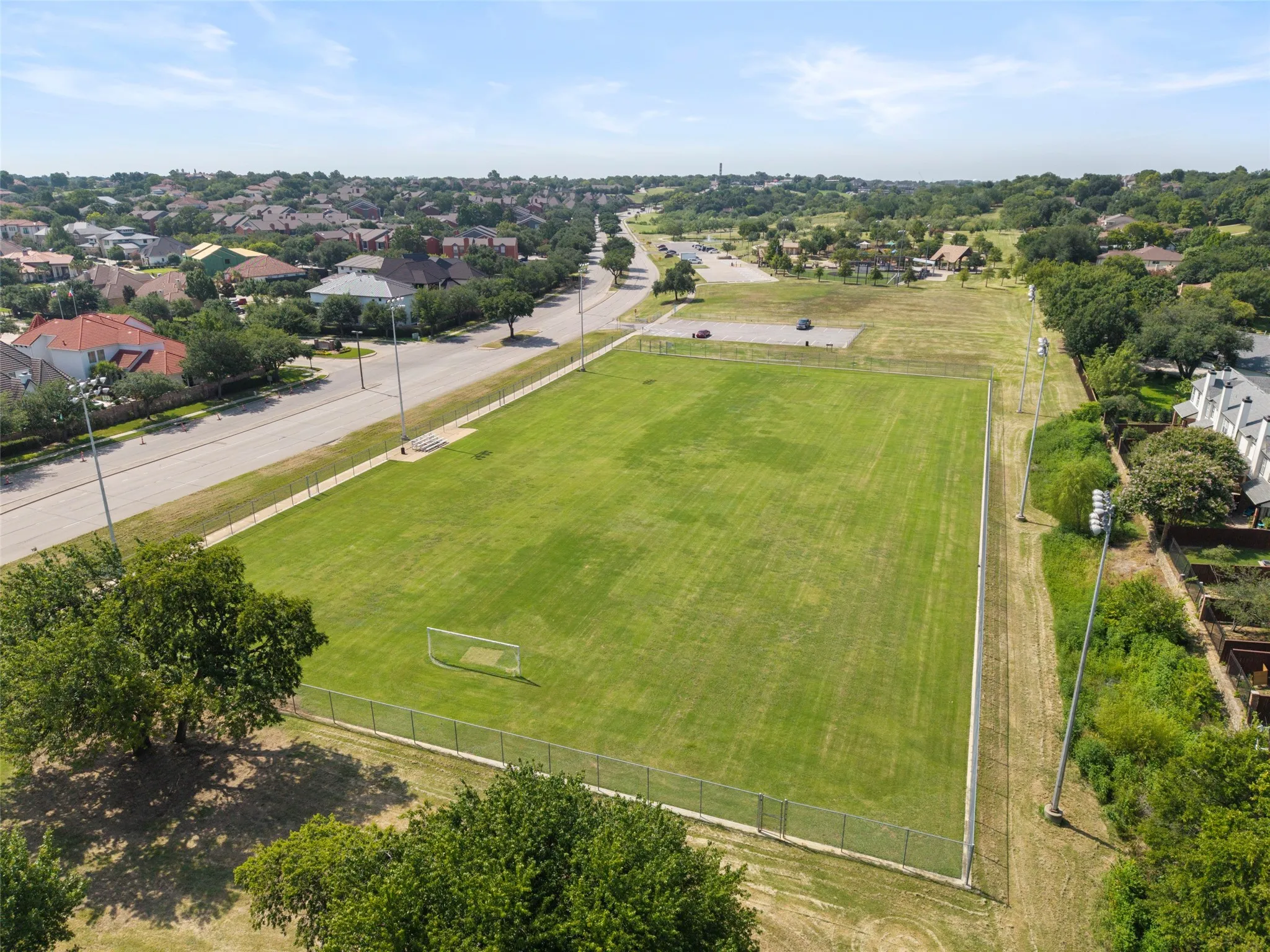 Expansive green field featuring a goalpost, surrounded by a fence and mature trees