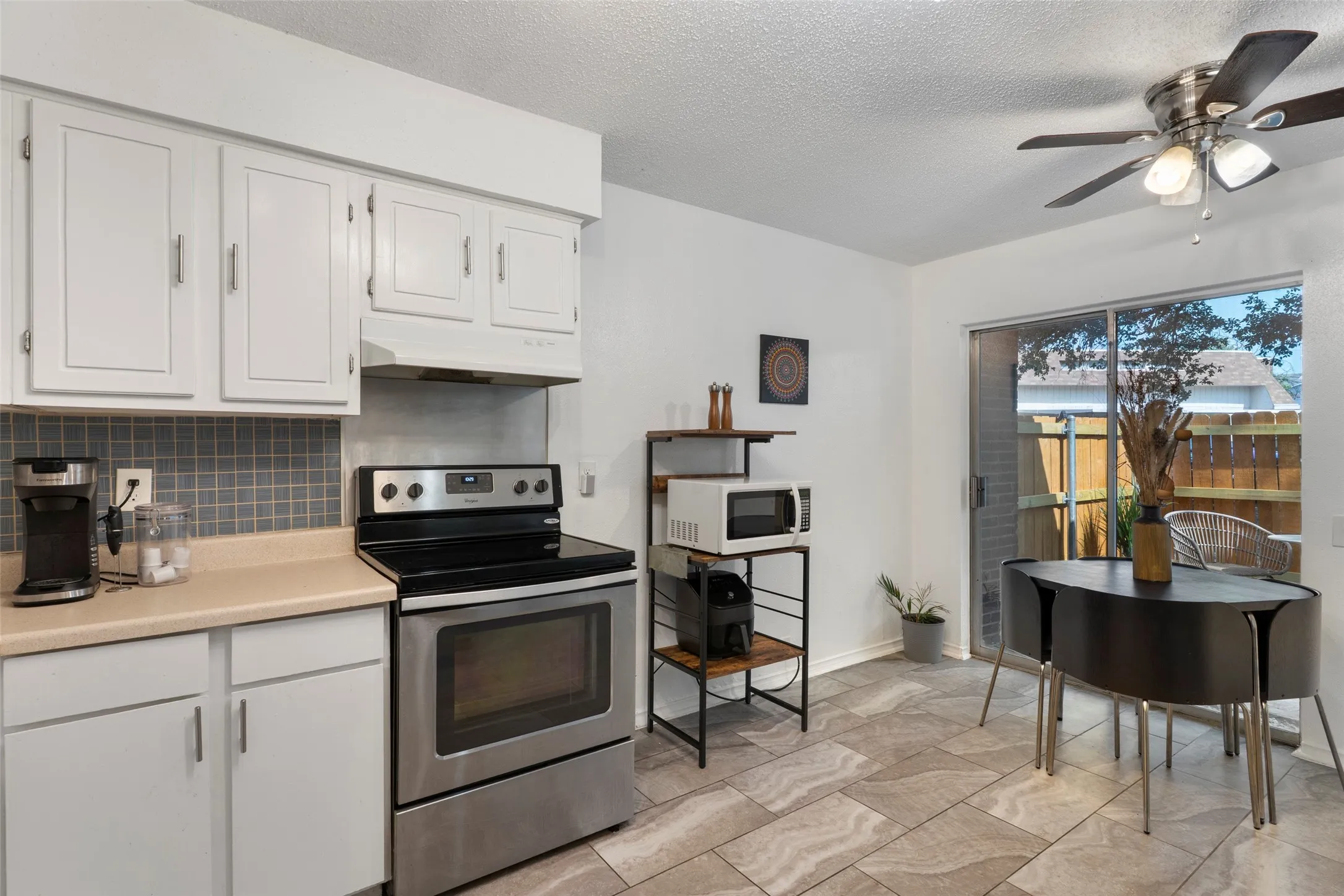 Open-concept kitchen and dining area featuring white cabinetry, stainless steel appliances including a black electric range and oven, light wood-finish countertops, gray tile backsplash, and ceramic tile flooring