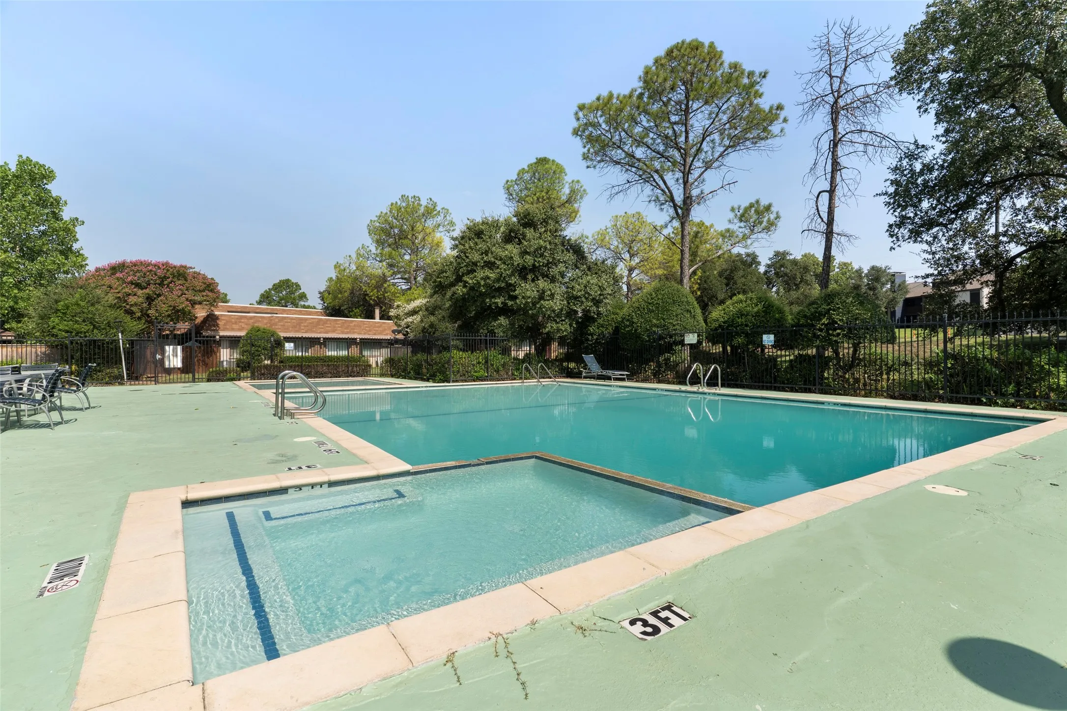 Swimming pool and spa with a concrete deck, surrounded by mature trees and fencing
