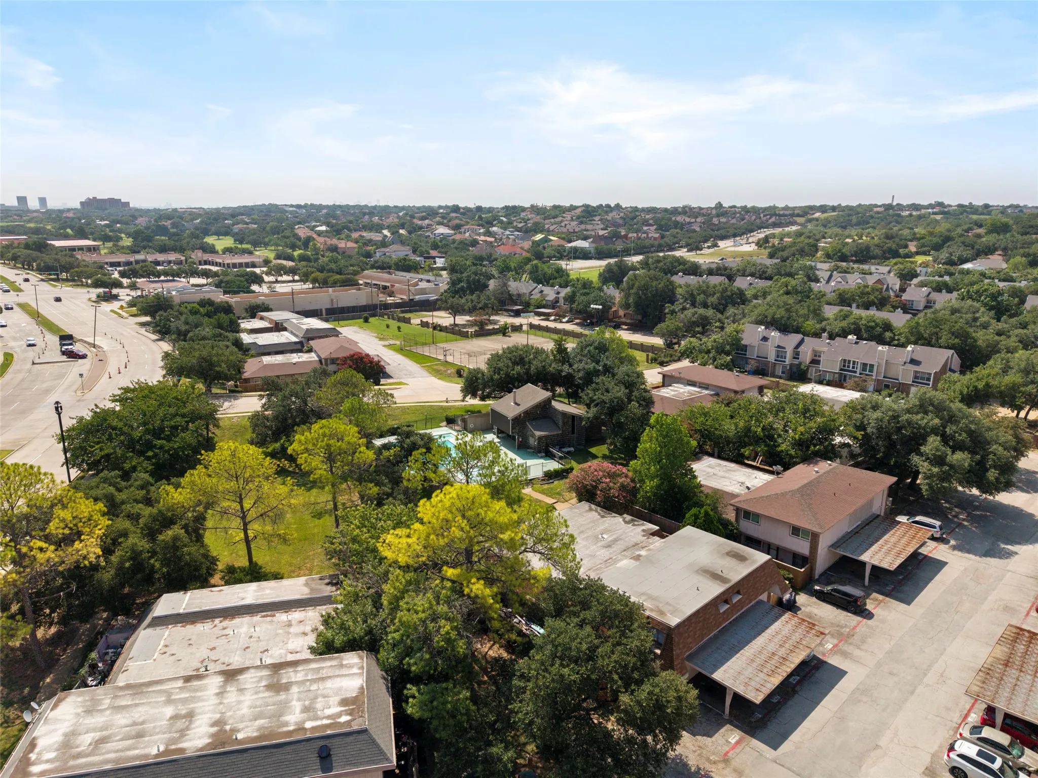 Expansive neighborhood setting with established landscaping, multiple residential structures, and a prominent roadway