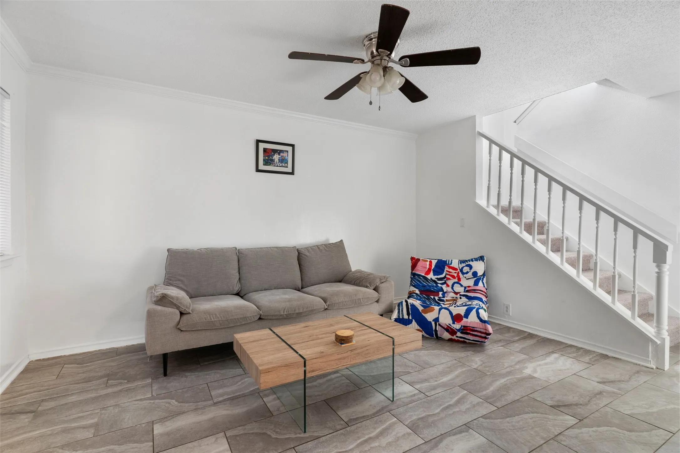 Bright loft-style space featuring exposed ceiling with ceiling fan, wood-finish flooring with geometric tile pattern, and a gray upholstered sofa