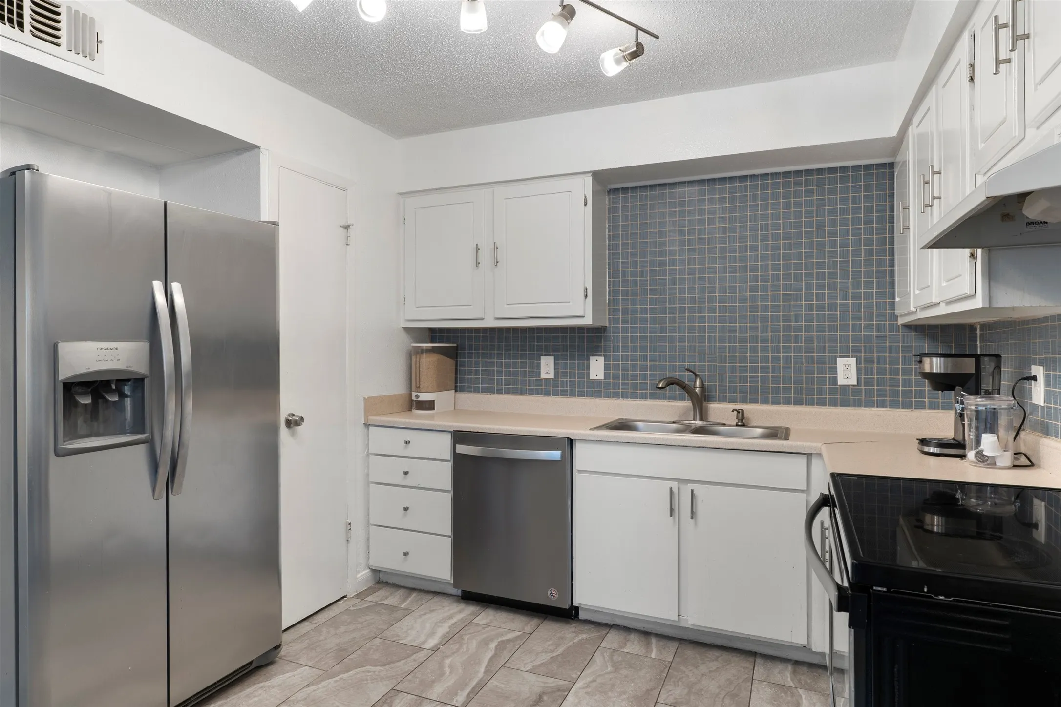 Kitchen featuring stainless steel appliances, white cabinetry, a tiled backsplash, and stone-look flooring
