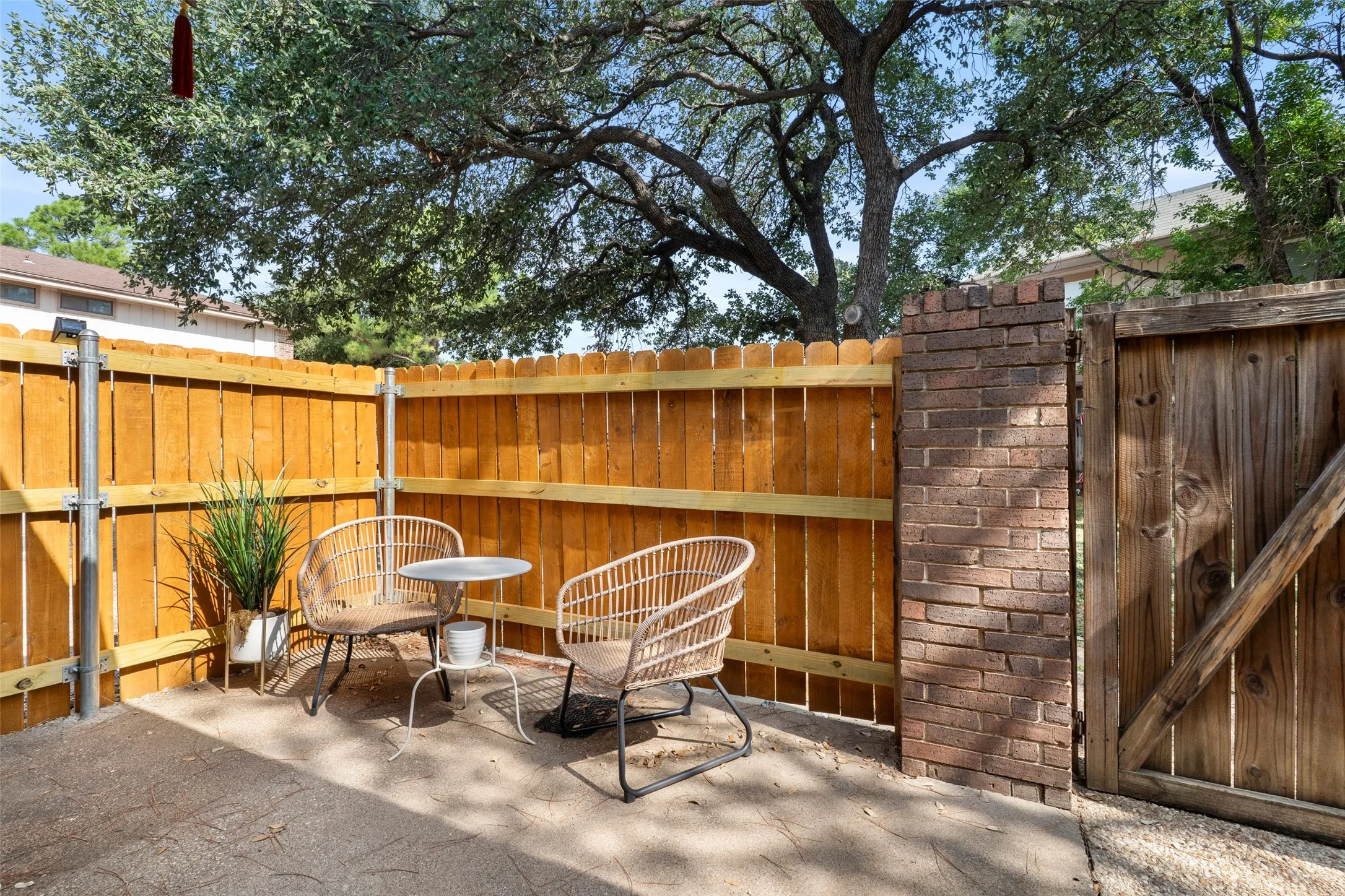 Private courtyard retreat featuring warm wood-finish fencing, mature shade trees, brick architectural detailing, and a gravel surface ideal for outdoor entertaining