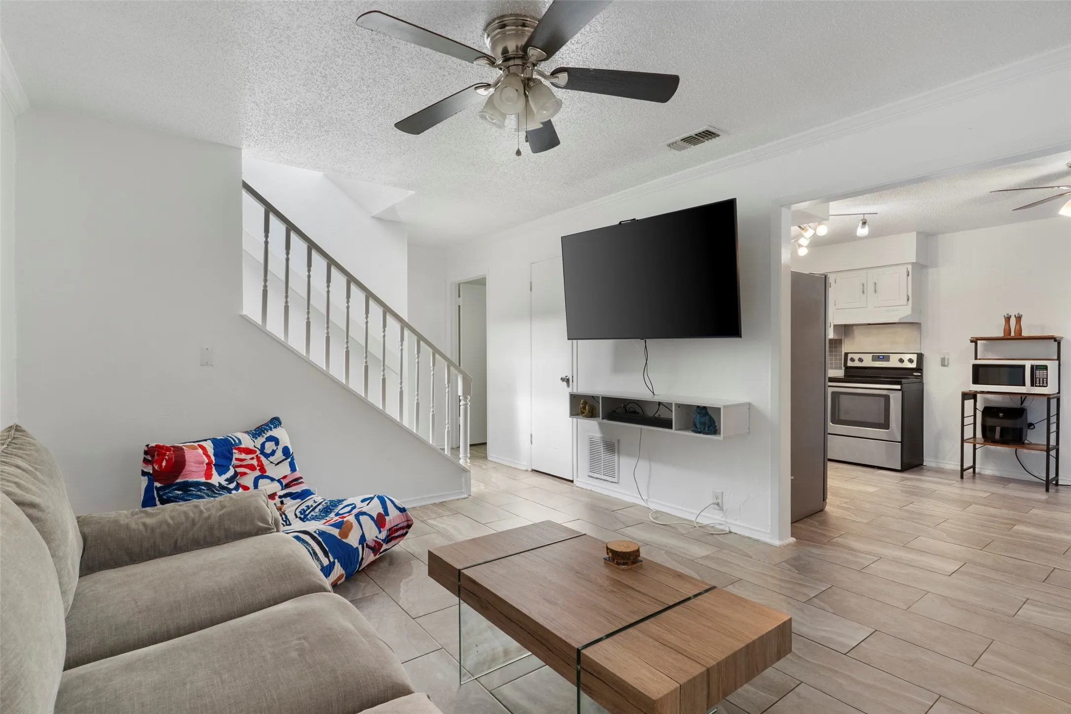 Open-concept living area featuring wood-finish flooring, a contemporary ceiling fan, and a built-in wall shelf