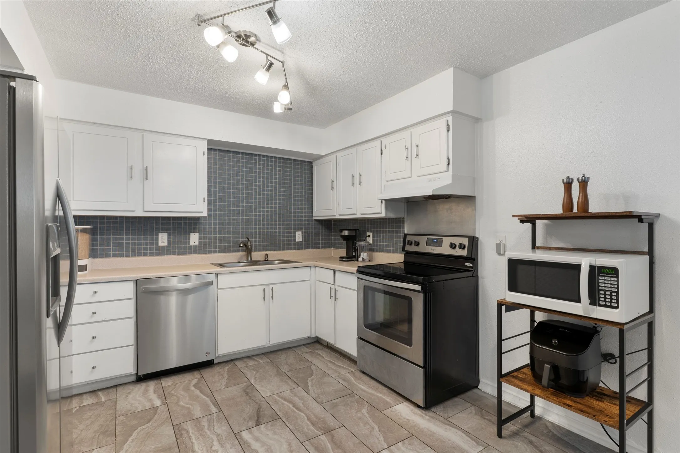 Modern kitchen featuring white cabinetry, stainless steel appliances including a dishwasher and electric range, gray subway tile backsplash, wood-finish flooring, and track lighting