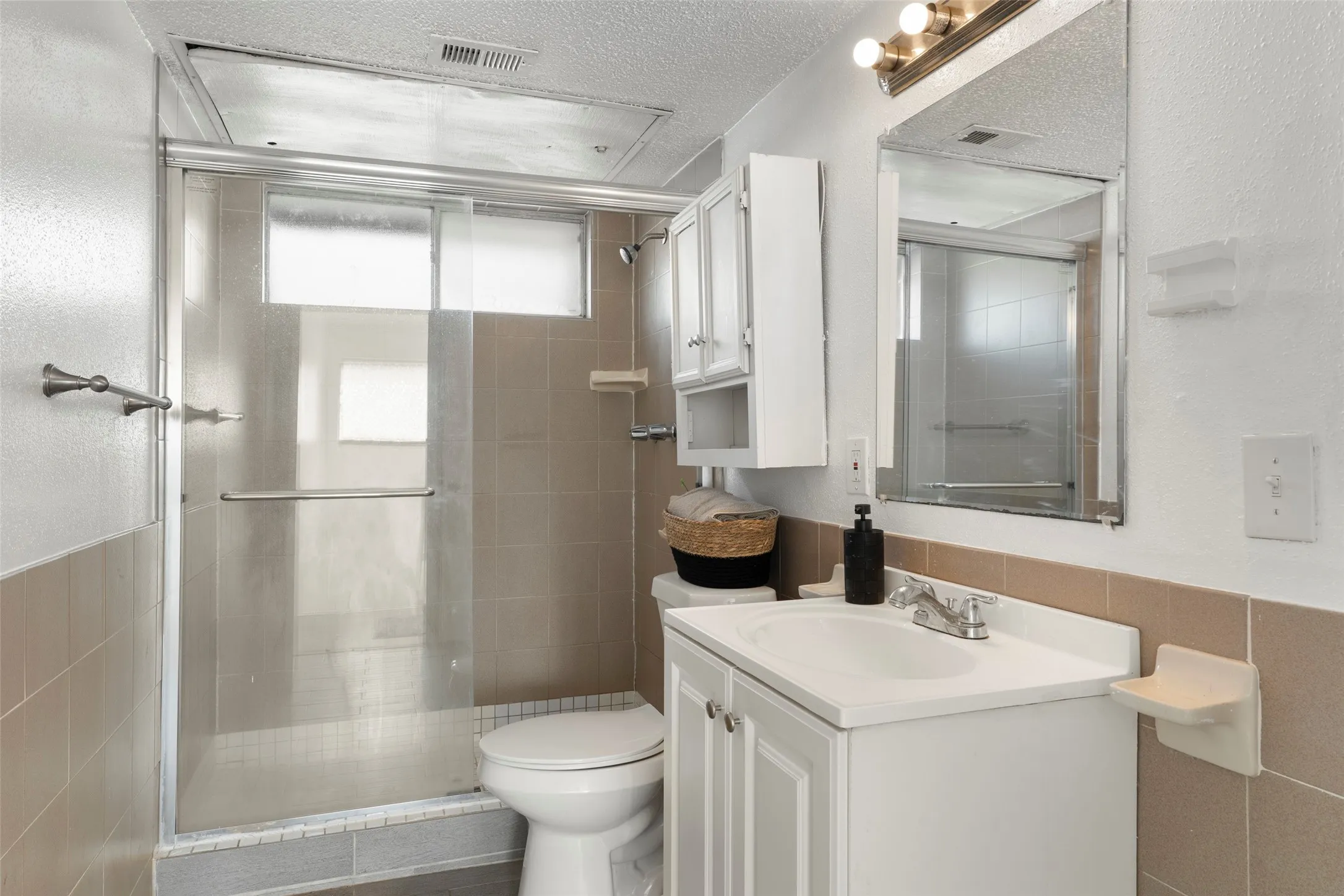 Bathroom featuring a vanity with an integrated sink, a mirrored medicine cabinet, and a shower with a sliding glass enclosure