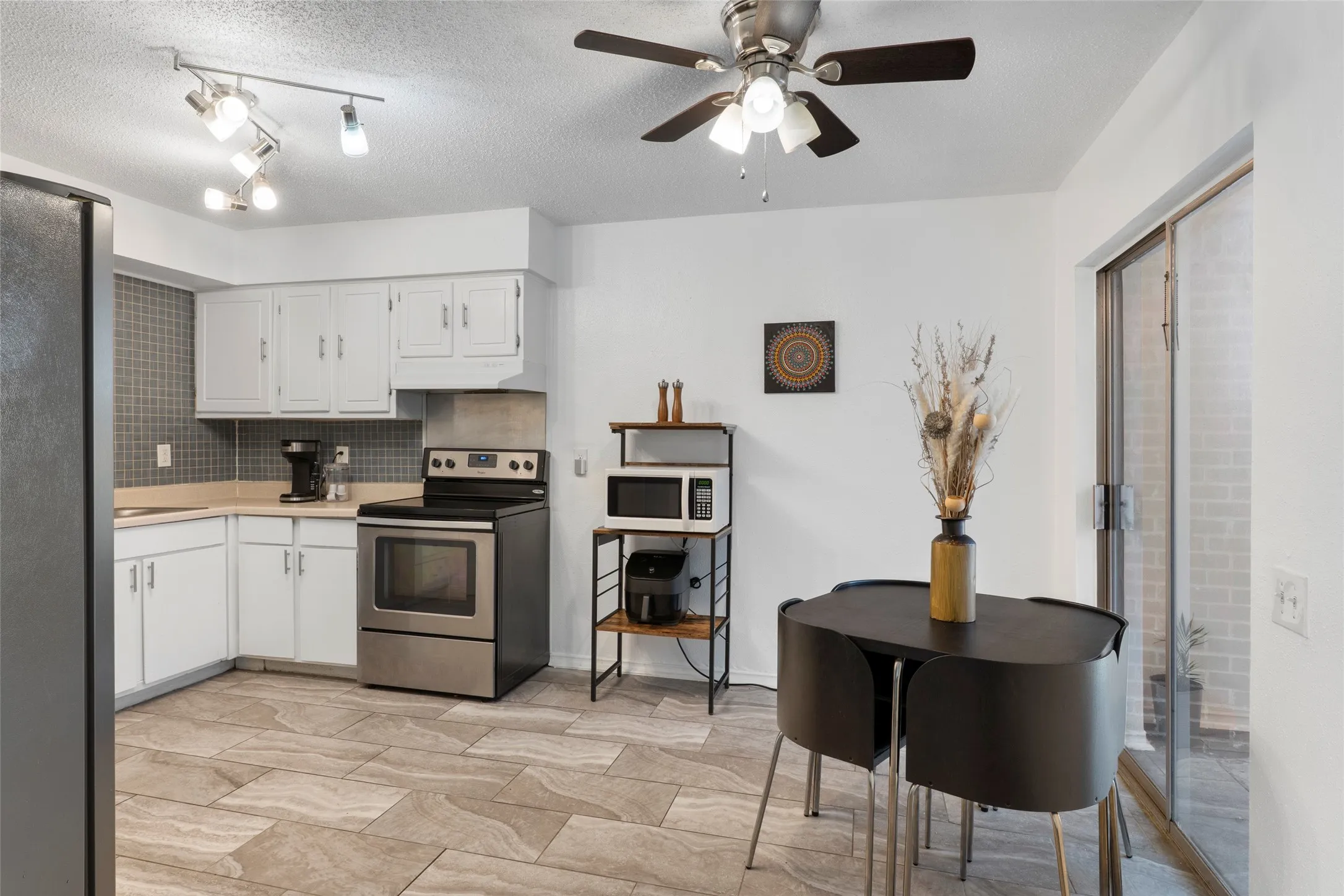 Kitchen featuring wood-finish tile flooring, white cabinetry, a tiled backsplash, stainless steel appliances, and a ceiling fan