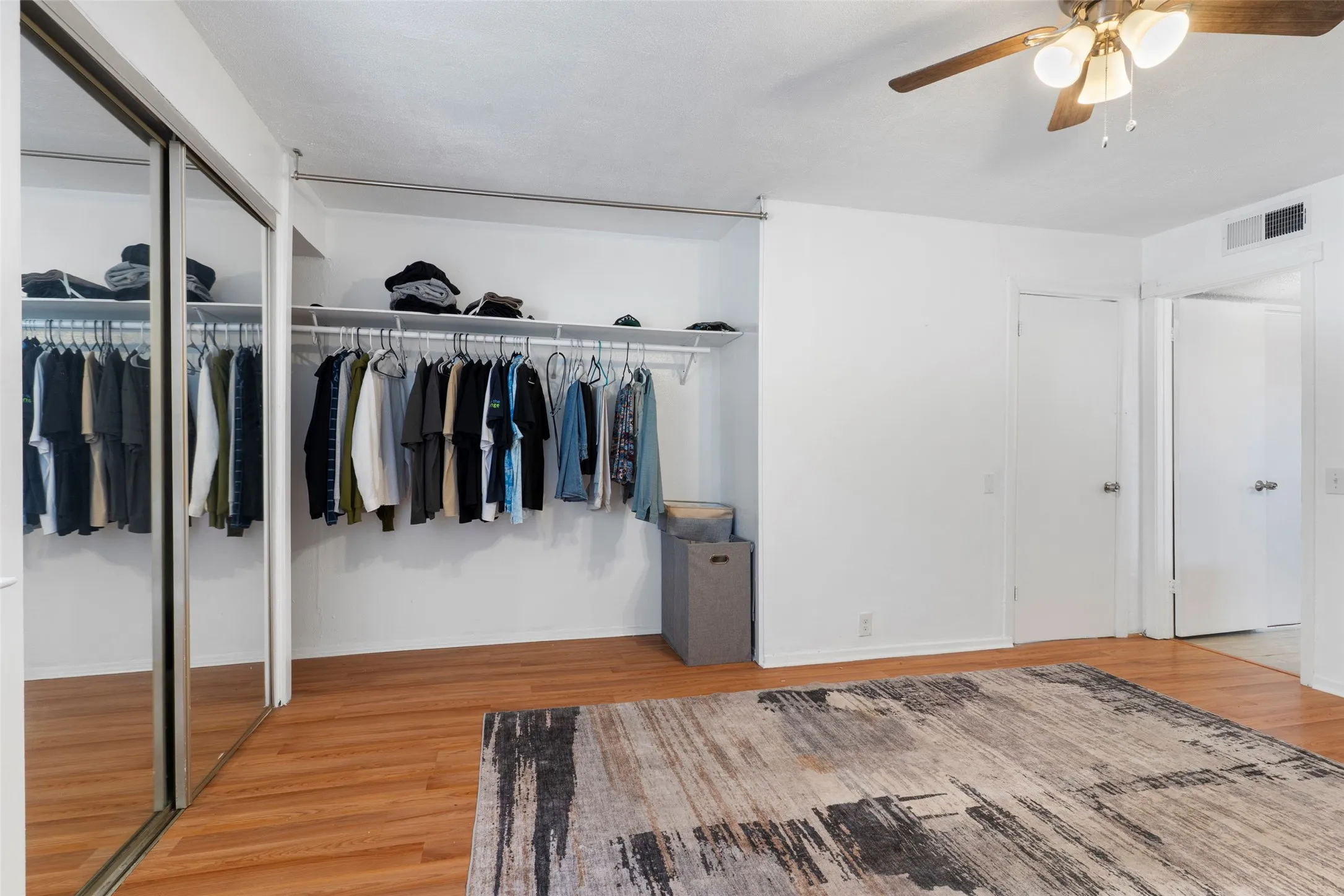 Primary Bedroom Suite with Mirrored Sliding-Door Closet, Hardwood Flooring, and Ceiling FanThis spacious bedroom features a large mirrored sliding-door closet system with extensive hanging storage and overhead shelving