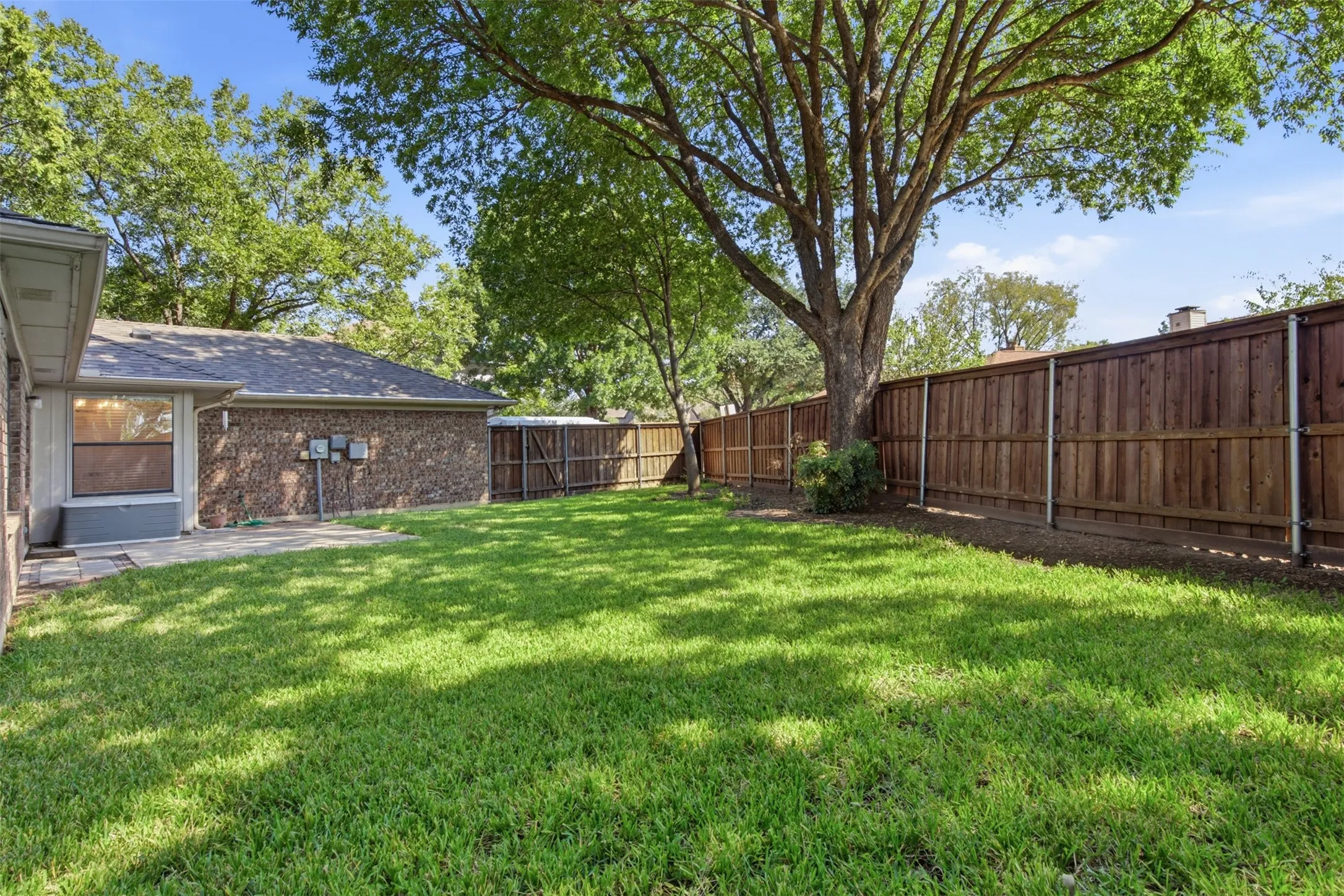 Expansive green lawn with a mature tree, stone patio, and a wood privacy fence