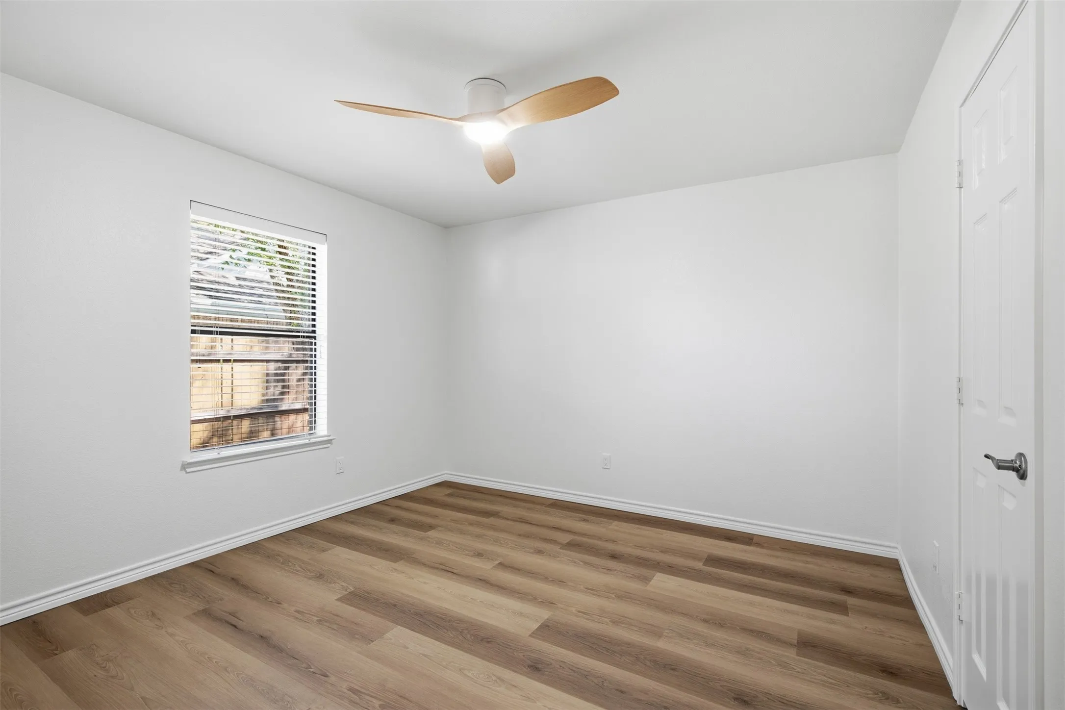 Wood-finish flooring, white painted walls, and a ceiling fan with light fixture