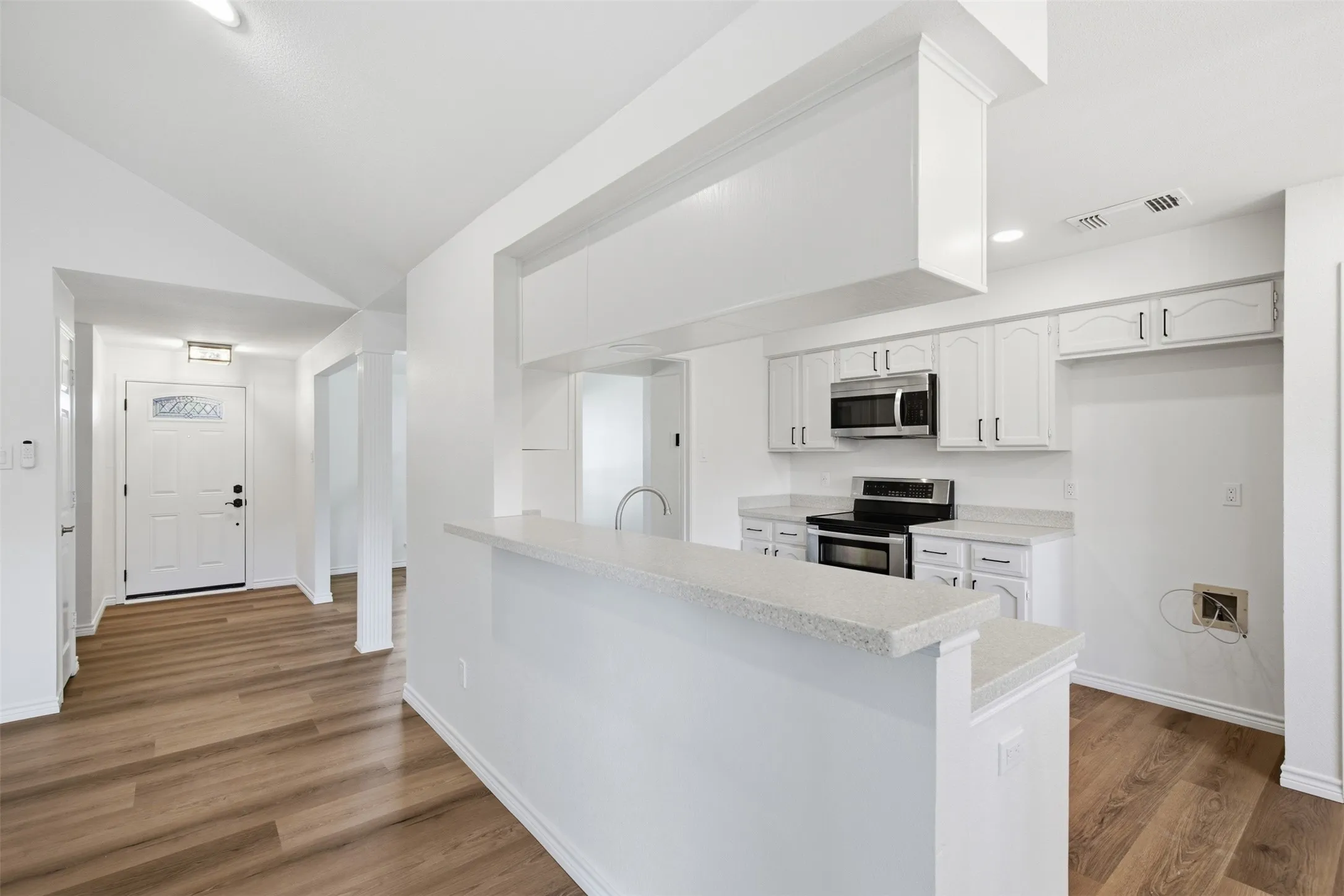 Kitchen featuring white cabinetry, stainless steel microwave, and range with a light-toned countertop