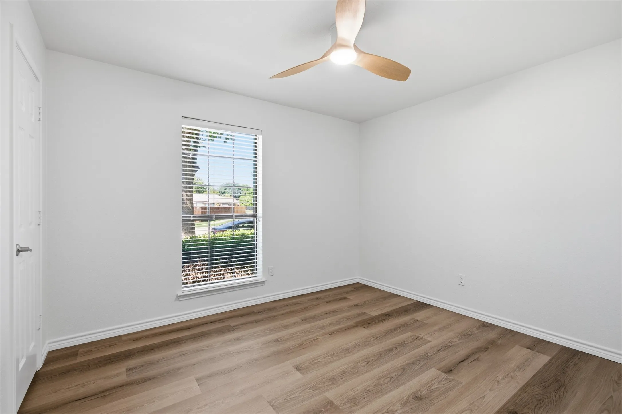 Expansive room featuring wood-finish flooring, a contemporary ceiling fan with integrated lighting, and a window equipped with blinds