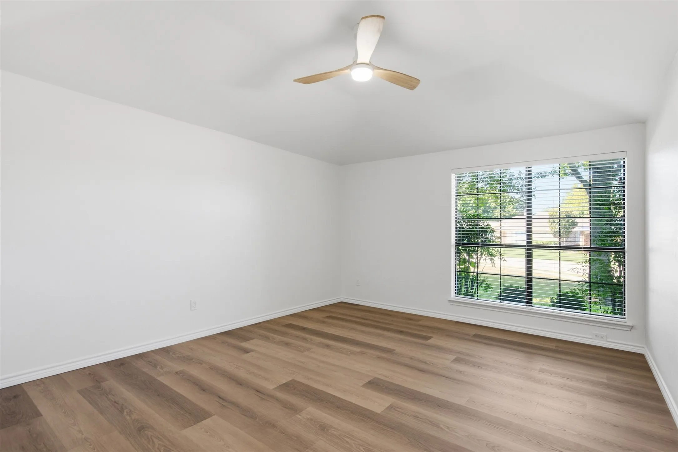 Bright corner bedroom featuring wood-finish plank flooring, abundant natural light from expansive multi-pane windows, and a modern ceiling fan with integrated lighting