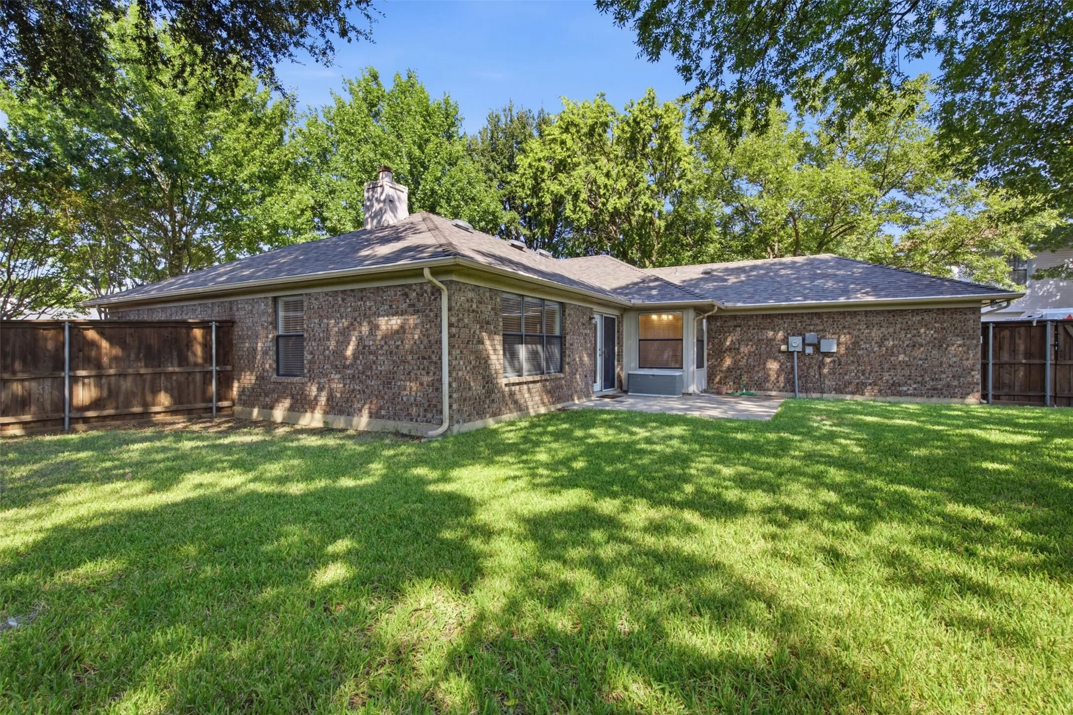 Spacious backyard featuring a manicured lawn, brick exterior, and a concrete patio