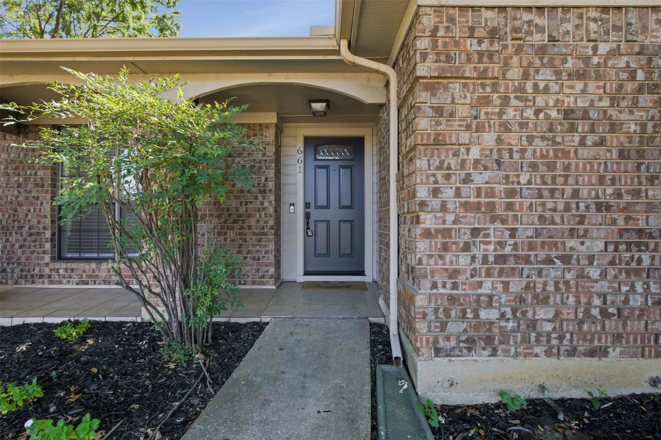 Brick exterior facade with a dark-paneled entry door, arched entryway, and covered front porch