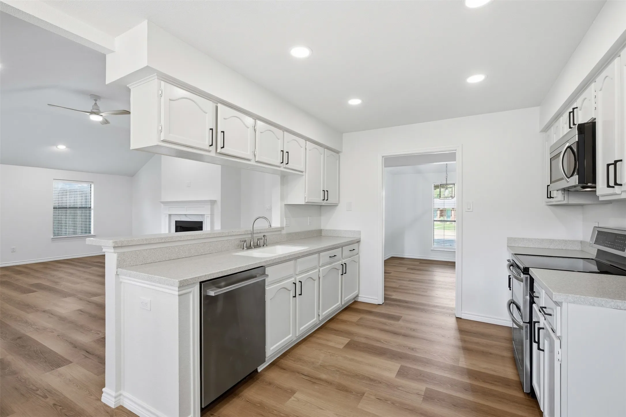 Open-concept kitchen with white cabinetry, stainless steel appliances, wood-finish flooring, and recessed lighting
