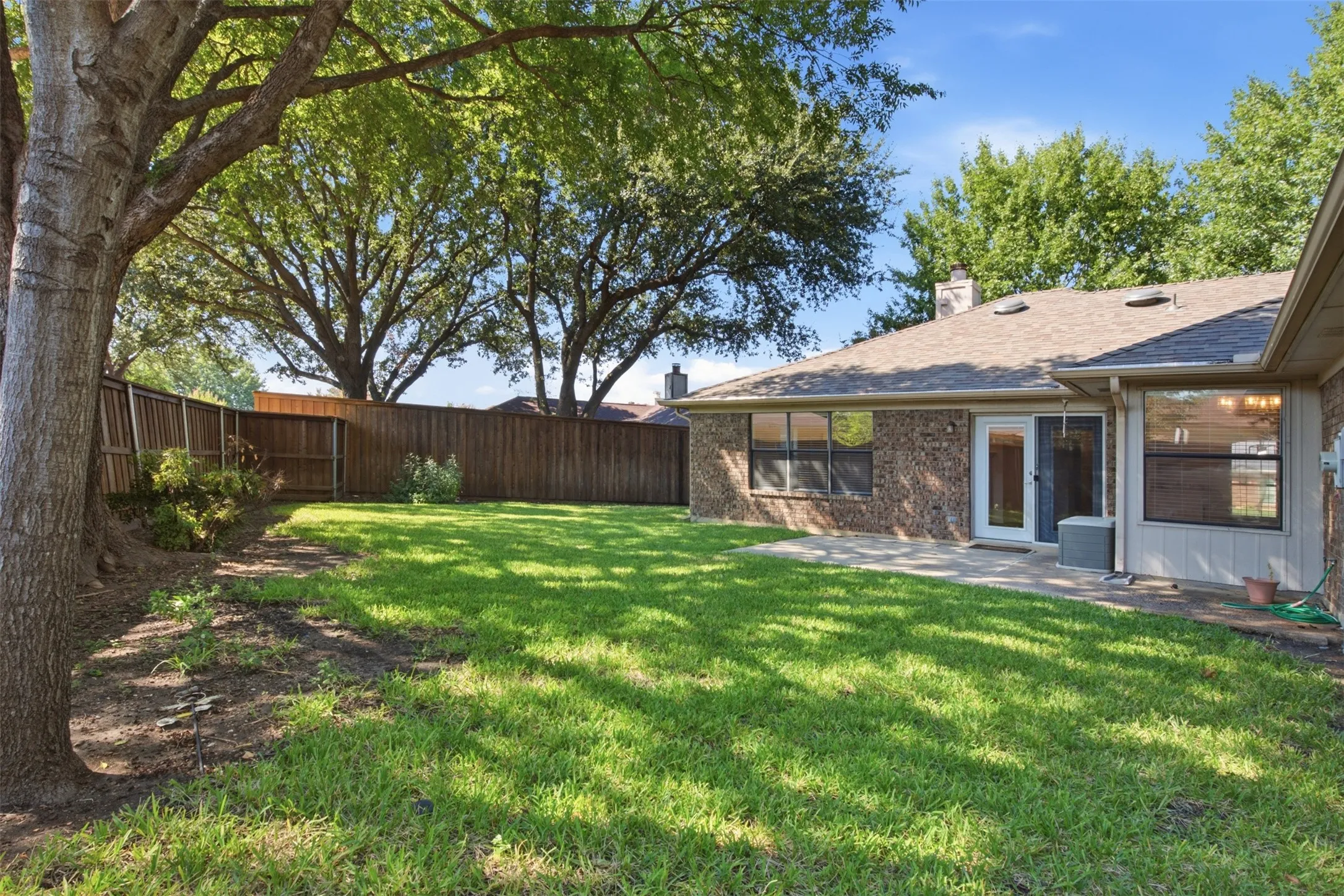 Expansive green lawn with mature trees, a privacy fence, and a patio area