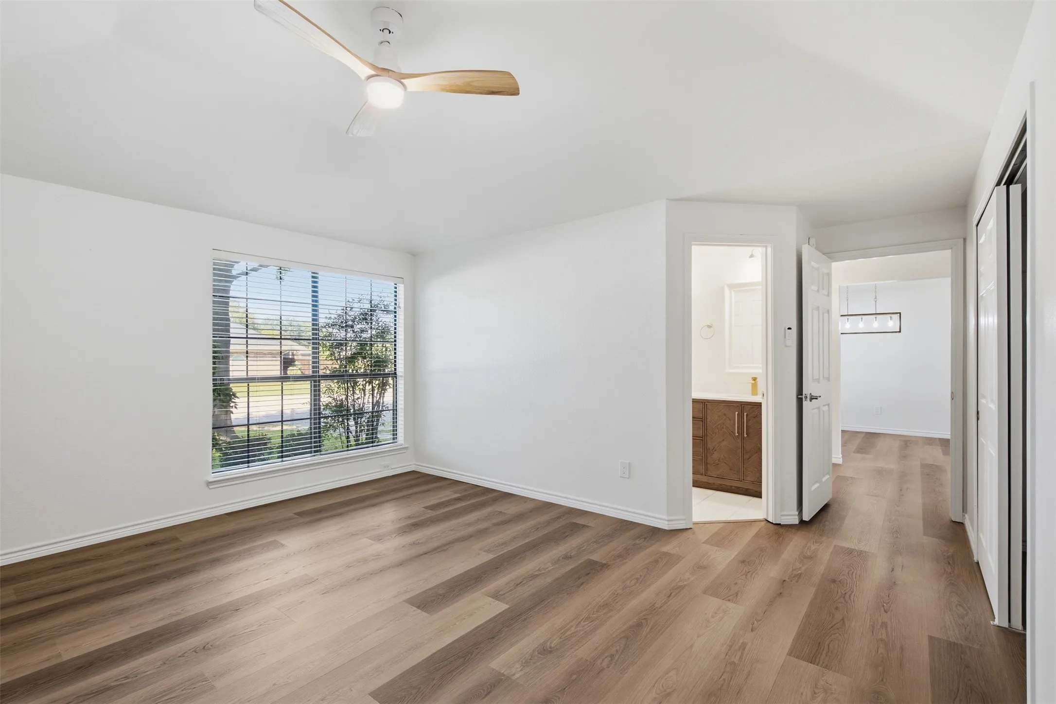 Wood-finish flooring throughout, bright white walls, and a window with blinds provide a neutral canvas