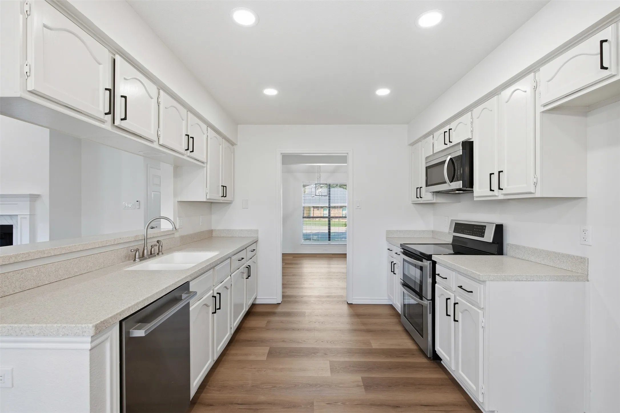 Galley kitchen featuring white cabinetry with brushed nickel hardware, stainless steel appliances including a double wall oven and built-in microwave, quartz countertops, and wood-finish flooring throughout