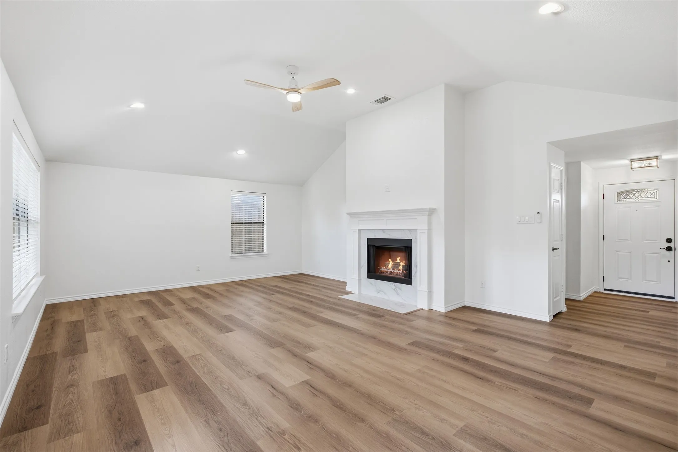 Vaulted ceiling, wood-finish flooring, recessed lighting, ceiling fan, and a fireplace with a mantel