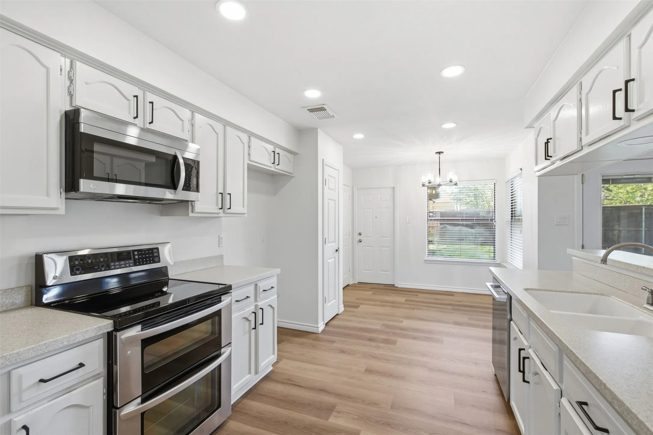 Kitchen featuring wood-finish flooring, white cabinetry with black hardware, stainless steel appliances, and recessed lighting