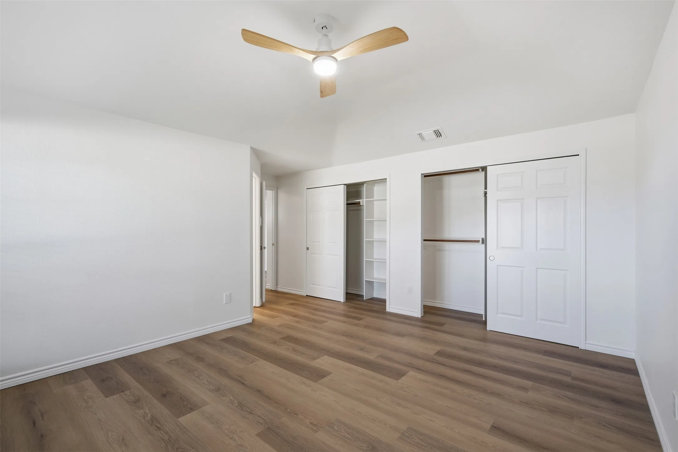 Vaulted ceiling, wood-finish flooring, ceiling fan with integrated lighting, built-in closet shelving, and sliding closet doors