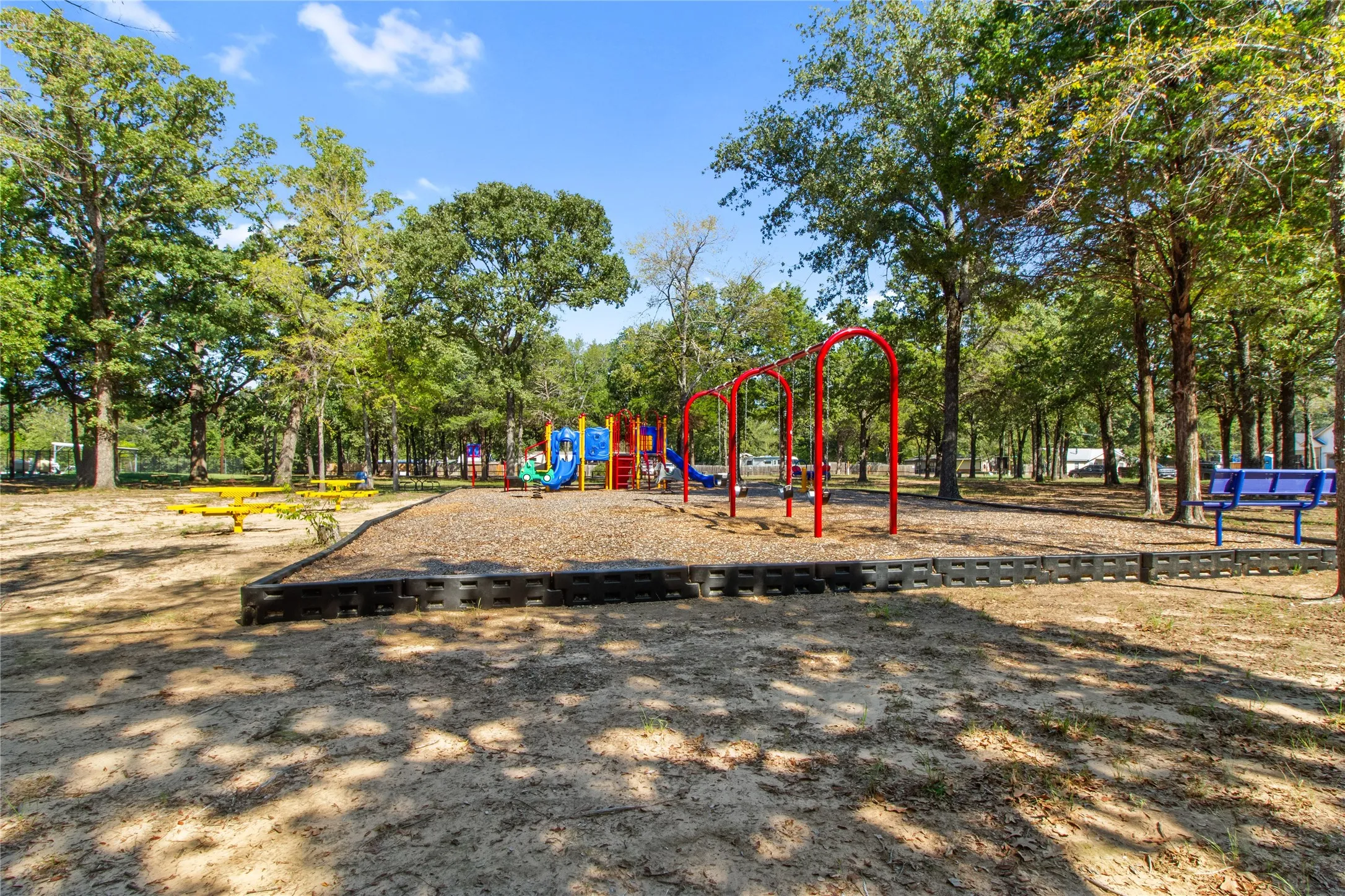 Outdoor recreation area featuring a playground with swings and slides, multiple picnic tables, and shaded seating