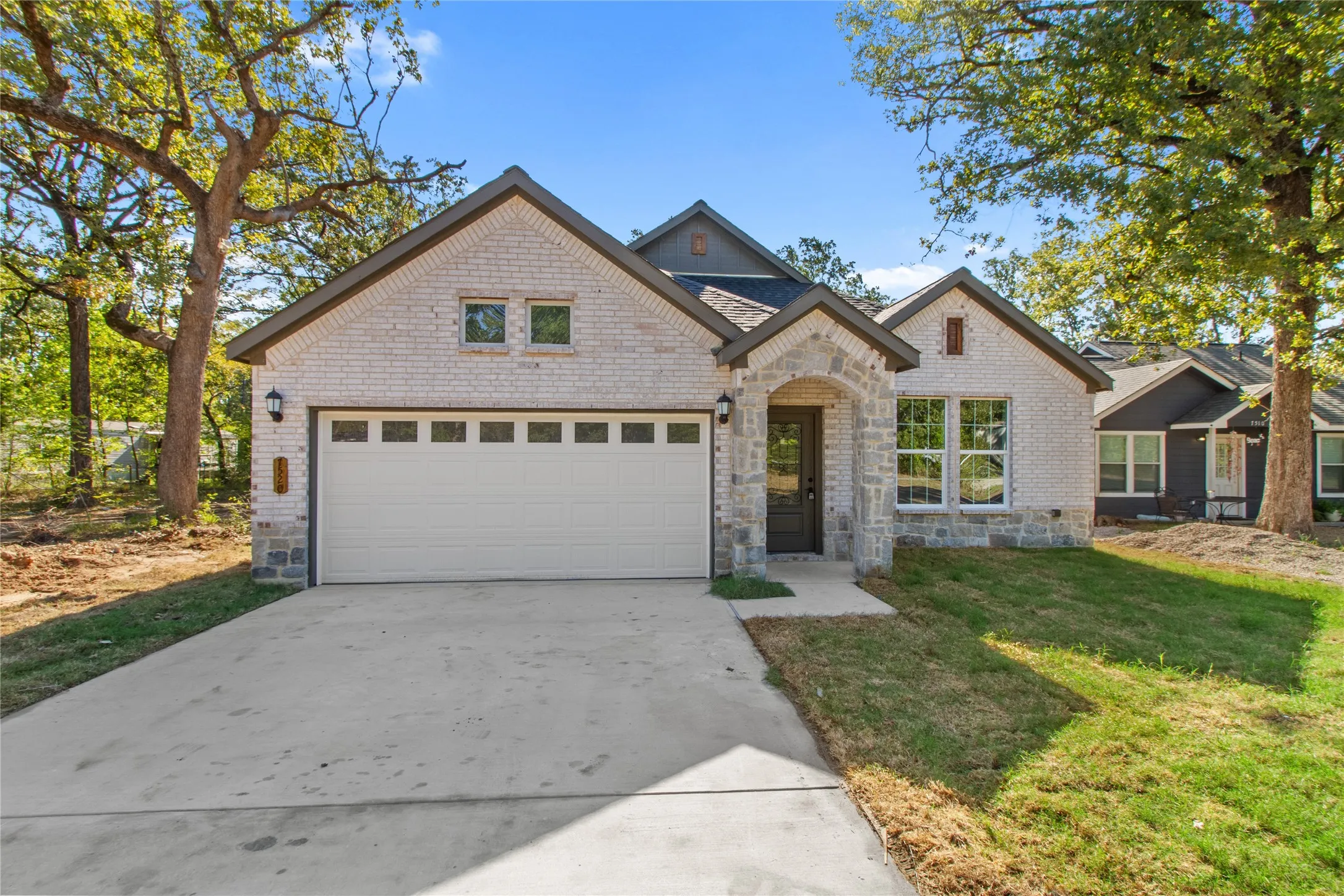 Contemporary home featuring a light-colored brick exterior, stone archway entry, dark framed windows, a two-car garage, and a concrete driveway