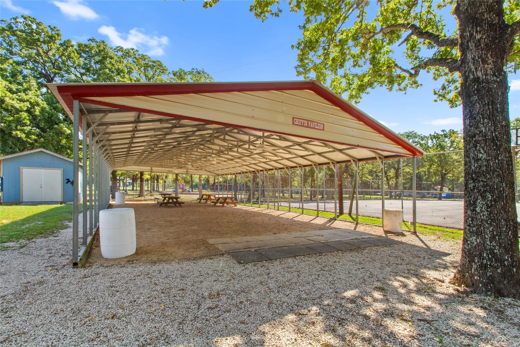 Expansive covered pavilion with red metal roof and open-sided design, providing ample shade over gravel grounds