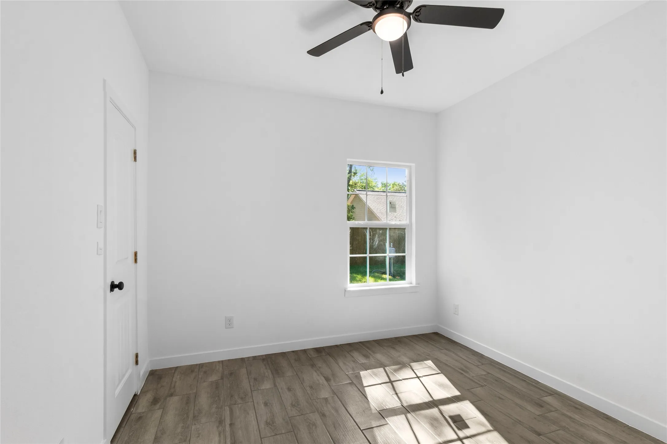 Wood-finish flooring with white baseboards, single window, and a ceiling fan with integrated lighting
