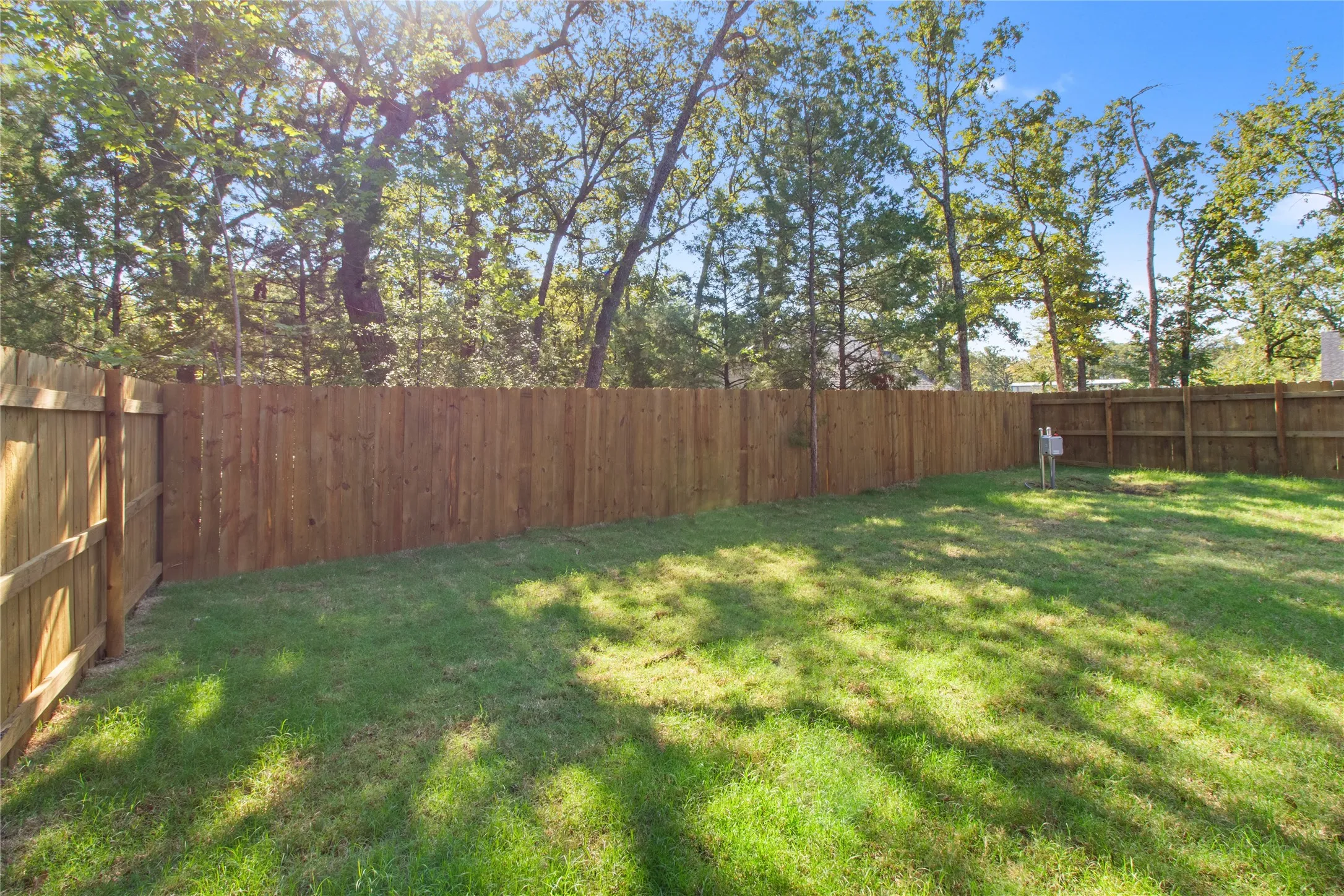 Expansive lawn area with a perimeter wood privacy fence, surrounded by mature trees