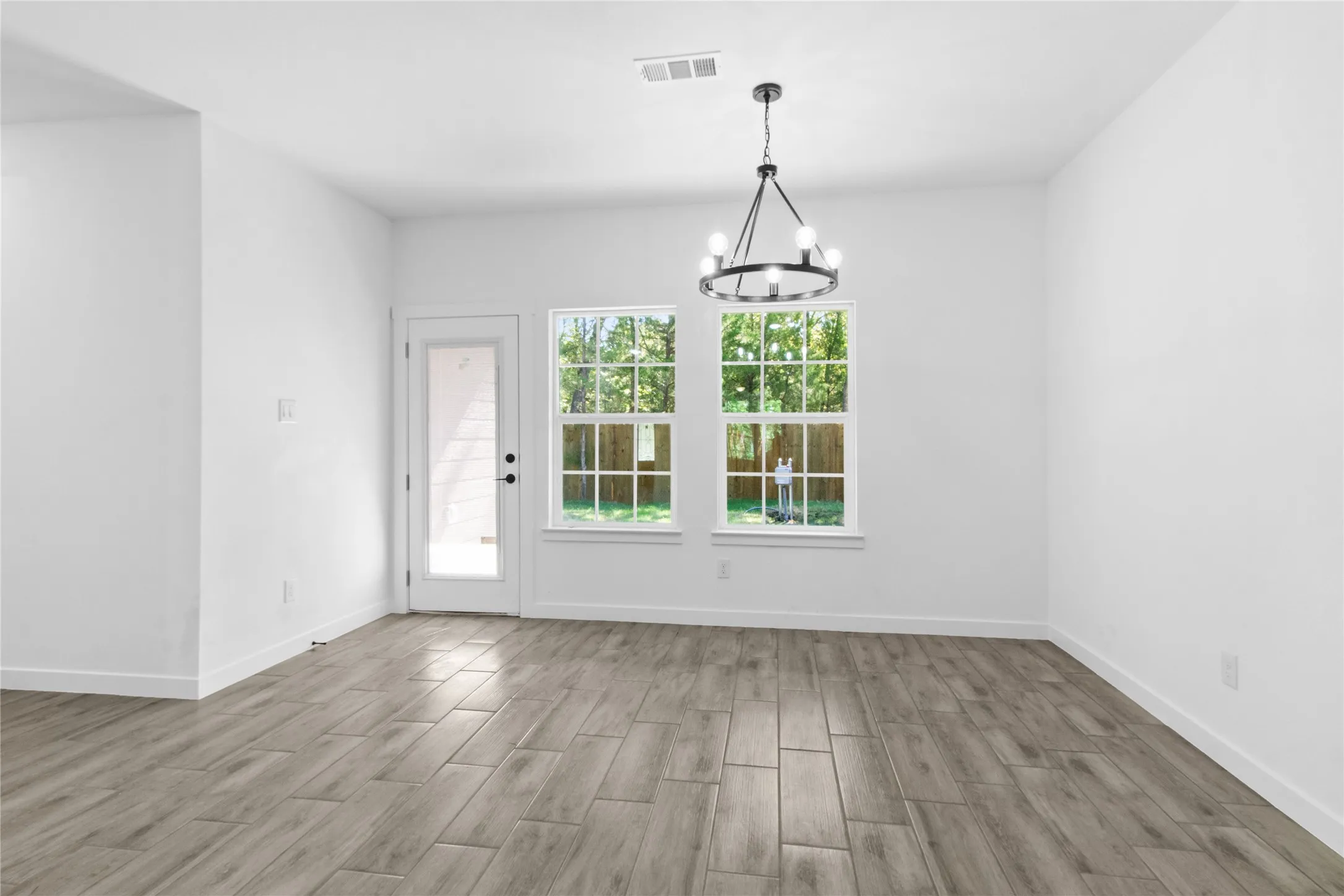 Wood-finish plank flooring, white walls, black chandelier, double-pane windows, and a glass-paneled exterior door