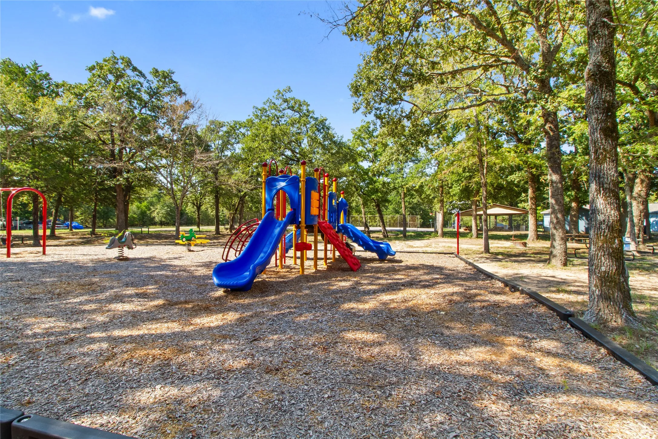 Playground area featuring a multi-slide play structure, swing set, and spring riders set on a wood chip surface