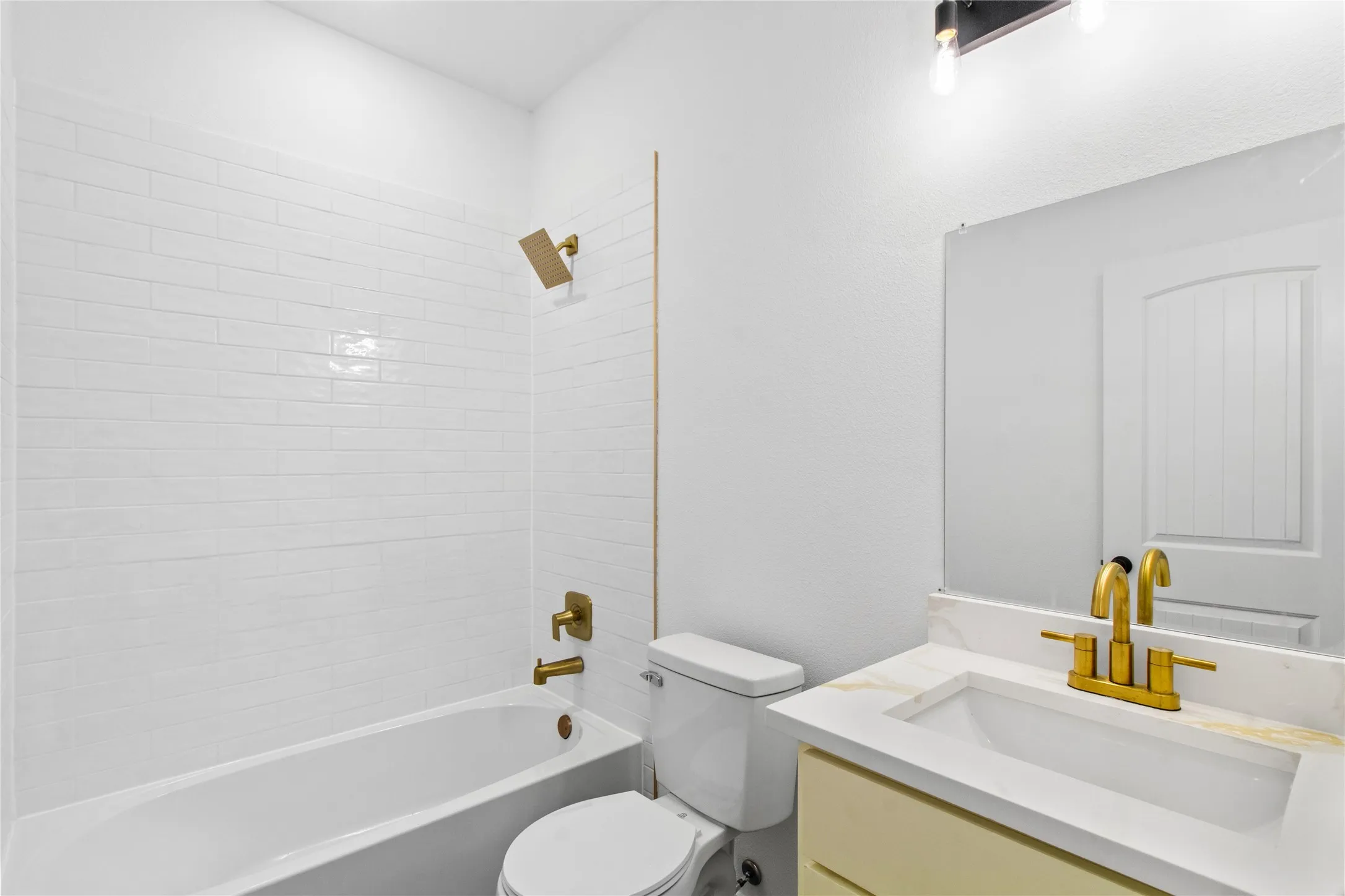 White subway tile tub surround featuring a gold-finish shower head and controls