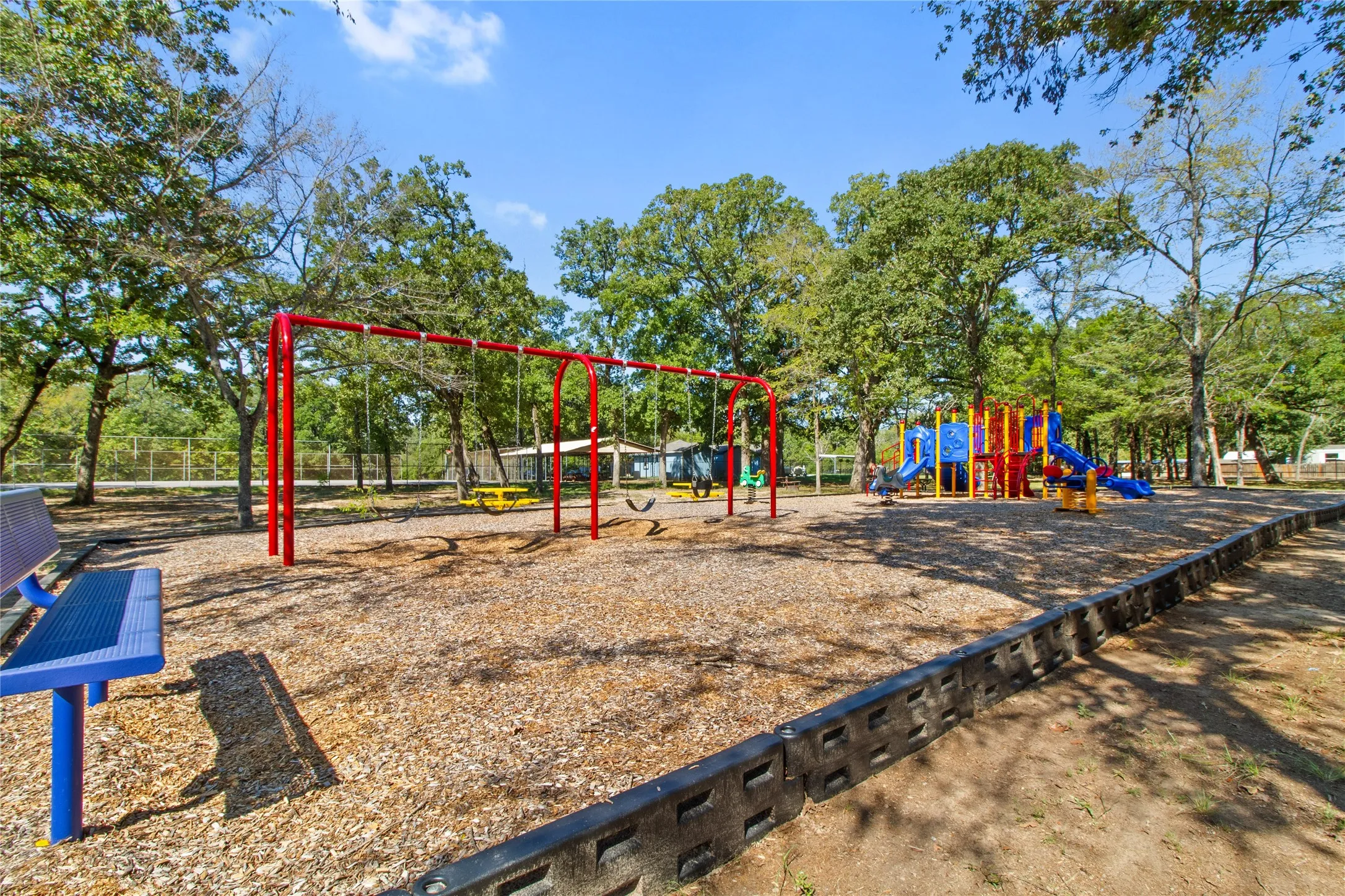 Playground featuring a swing set, slides, and recreational structures over wood chip surfacing, bordered by a concrete retaining wall