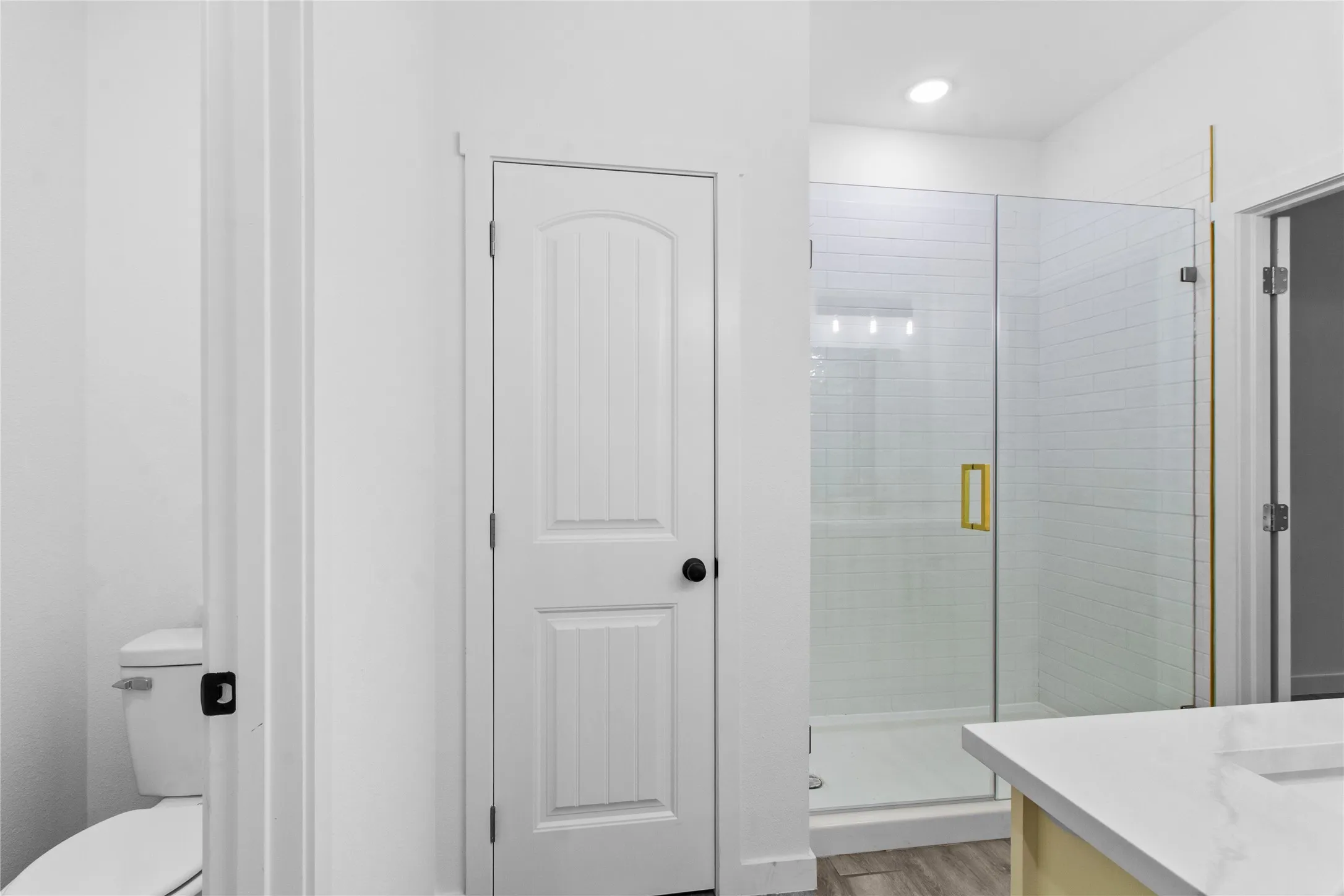 Glass-enclosed shower with subway tile surround, white solid-surface countertop, and gold-finish hardware