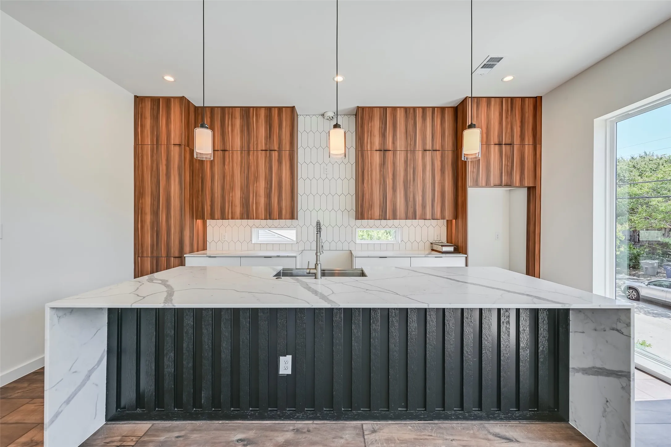 Waterfall island with a patterned countertop, wood-finish cabinetry, recessed lighting, drop pendant lighting, and a window for natural light