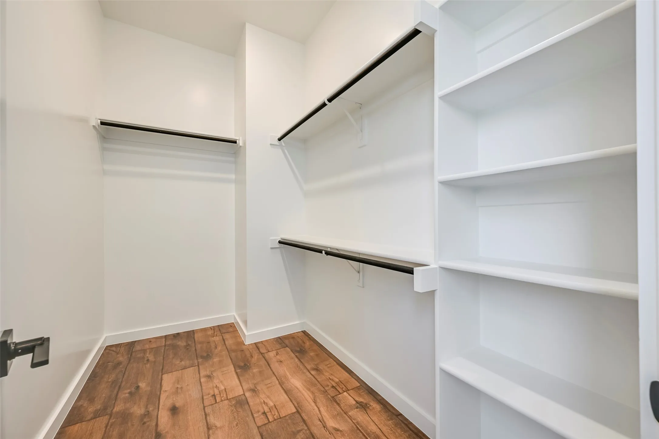 Wood-finish flooring with white walls, multiple built-in shelving units, and black clothing rods