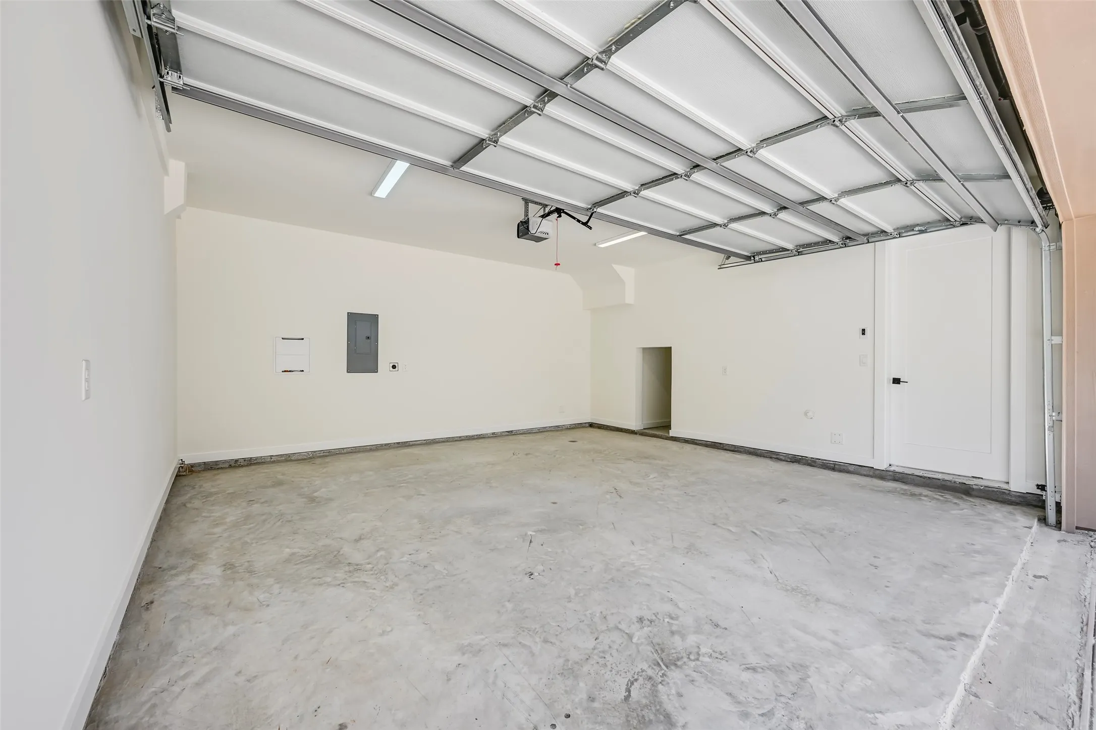Two-car garage with concrete flooring, automatic garage door opener, recessed lighting, and a utility door