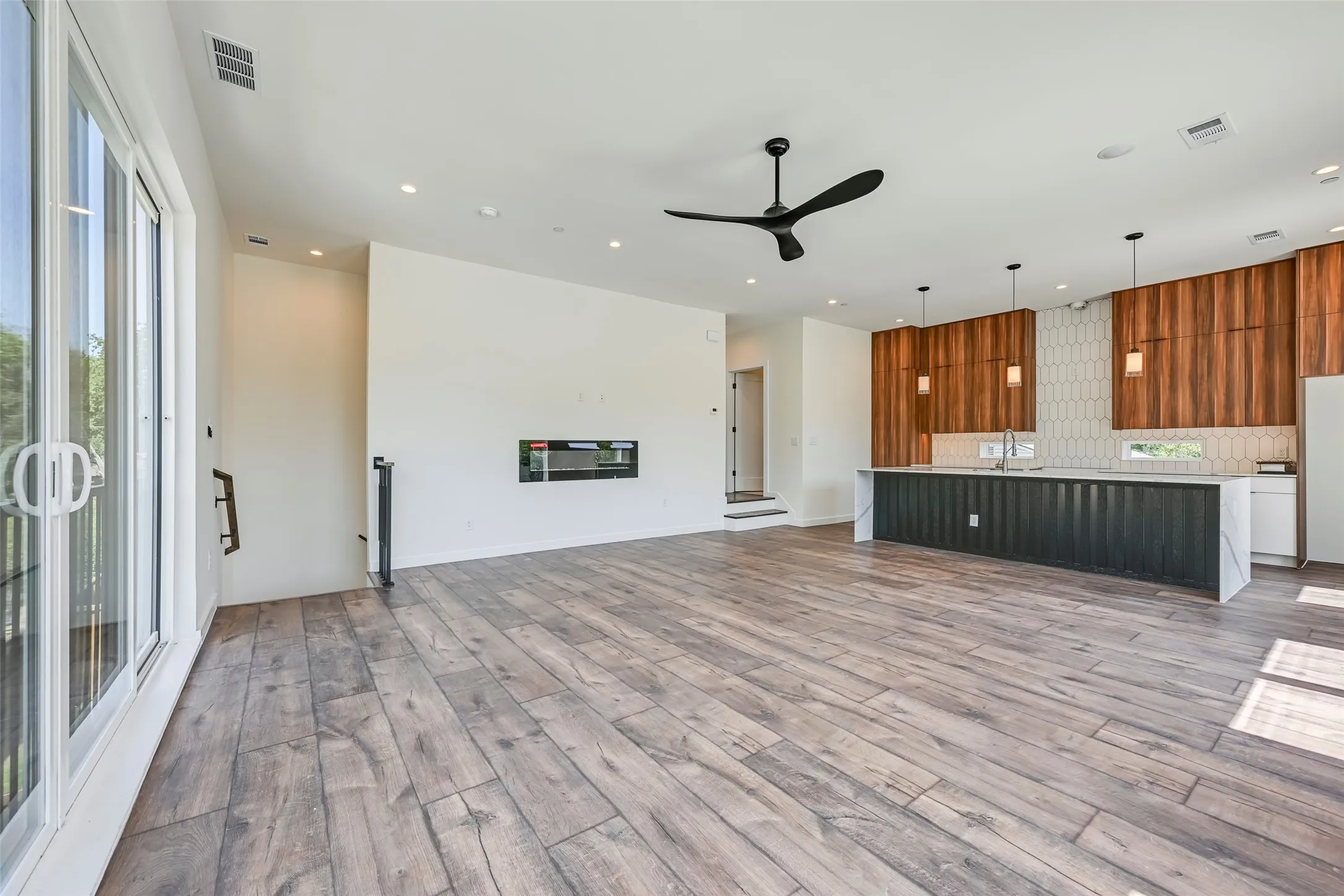 Spacious open-concept living area featuring wood-finish flooring, a linear electric fireplace, and a modern ceiling fan